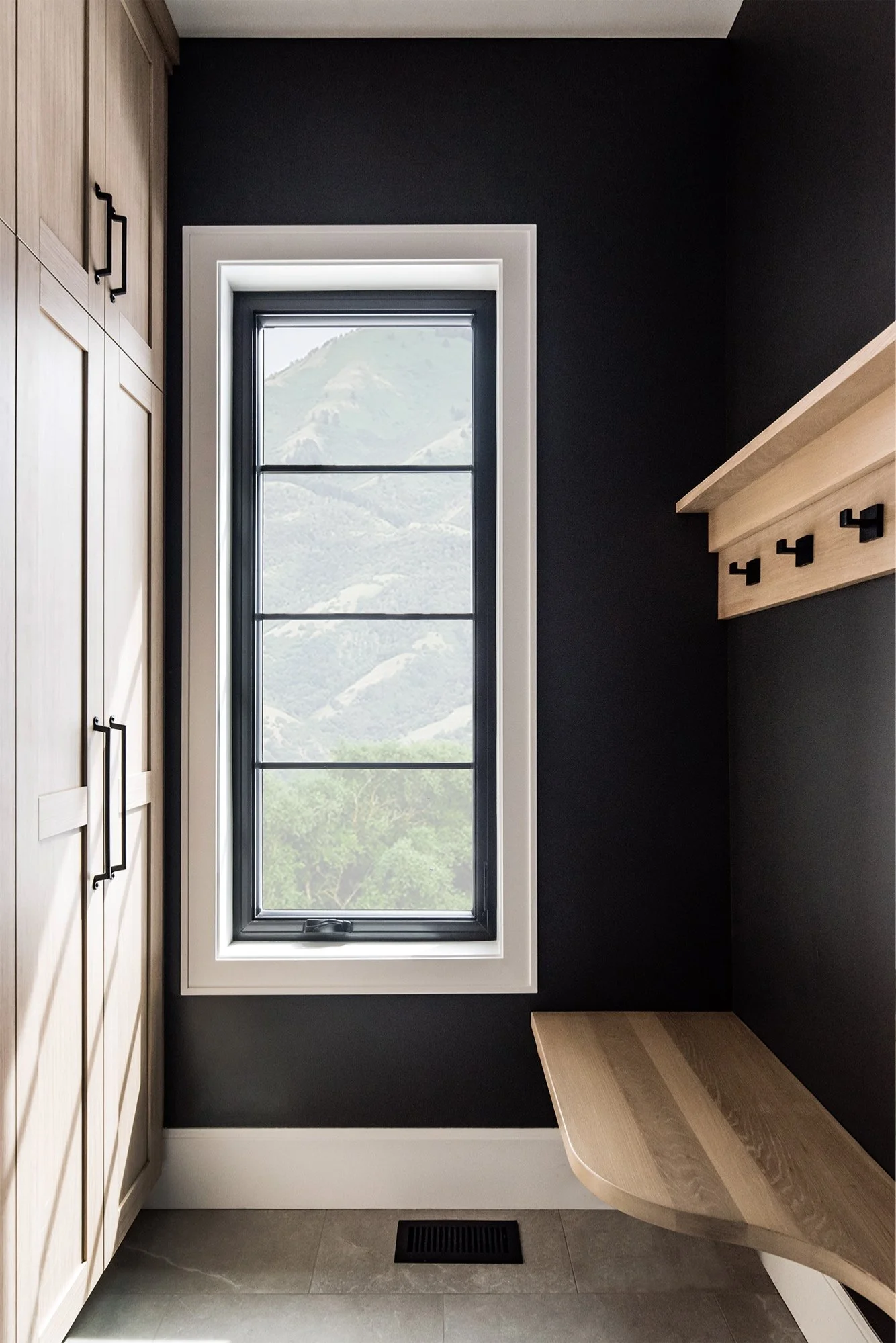 Mud room with black walls, a wooden bench and locker space designed by Liz Powell Design in Logan, UT. mud room modern #LizPowellDesign #interiordesignerscachevalley #loganinteriordesigners #buildingvsremodeling #modernhouses #northernutahinteriors