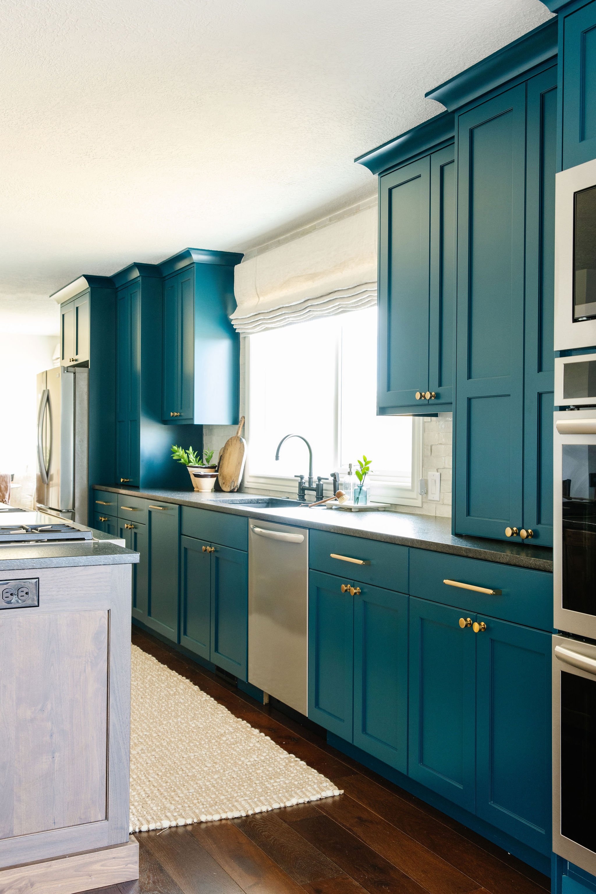  This modern kitchen features teal cabinets with gold handles designed by Logan, Utah interior designer Liz Powell. Teal cabinets gold hardware roman shades crown molding #colorfulcabinets #romanshades #modernkitchen #interiordesignkitchen 