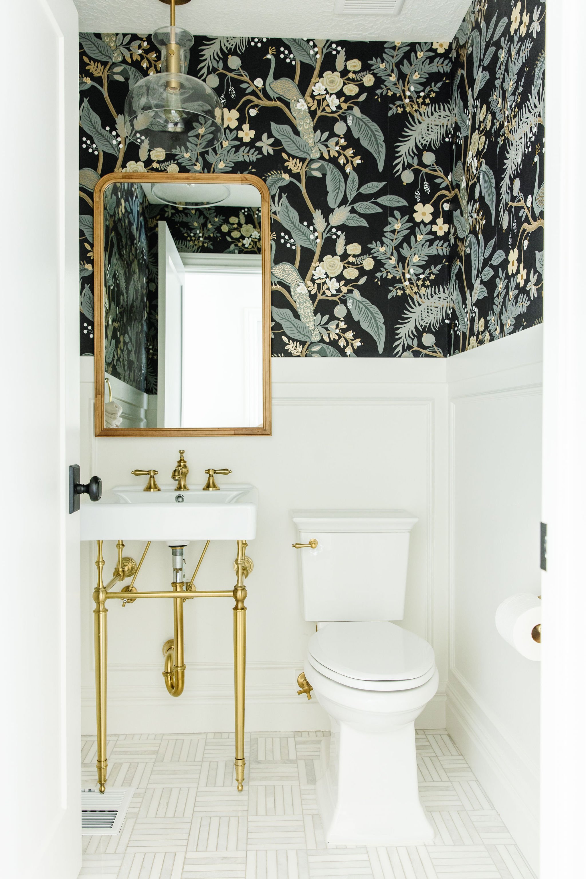  Liz Powell combined vibrant wallpaper with peaceful wainscotting to enhance the effect of this small power bathroom. Small space color gold bath figures and pipes patterned tile #bathroomwallpaper #smallbathroom #blackandgreenwallpaper #exposedpipes