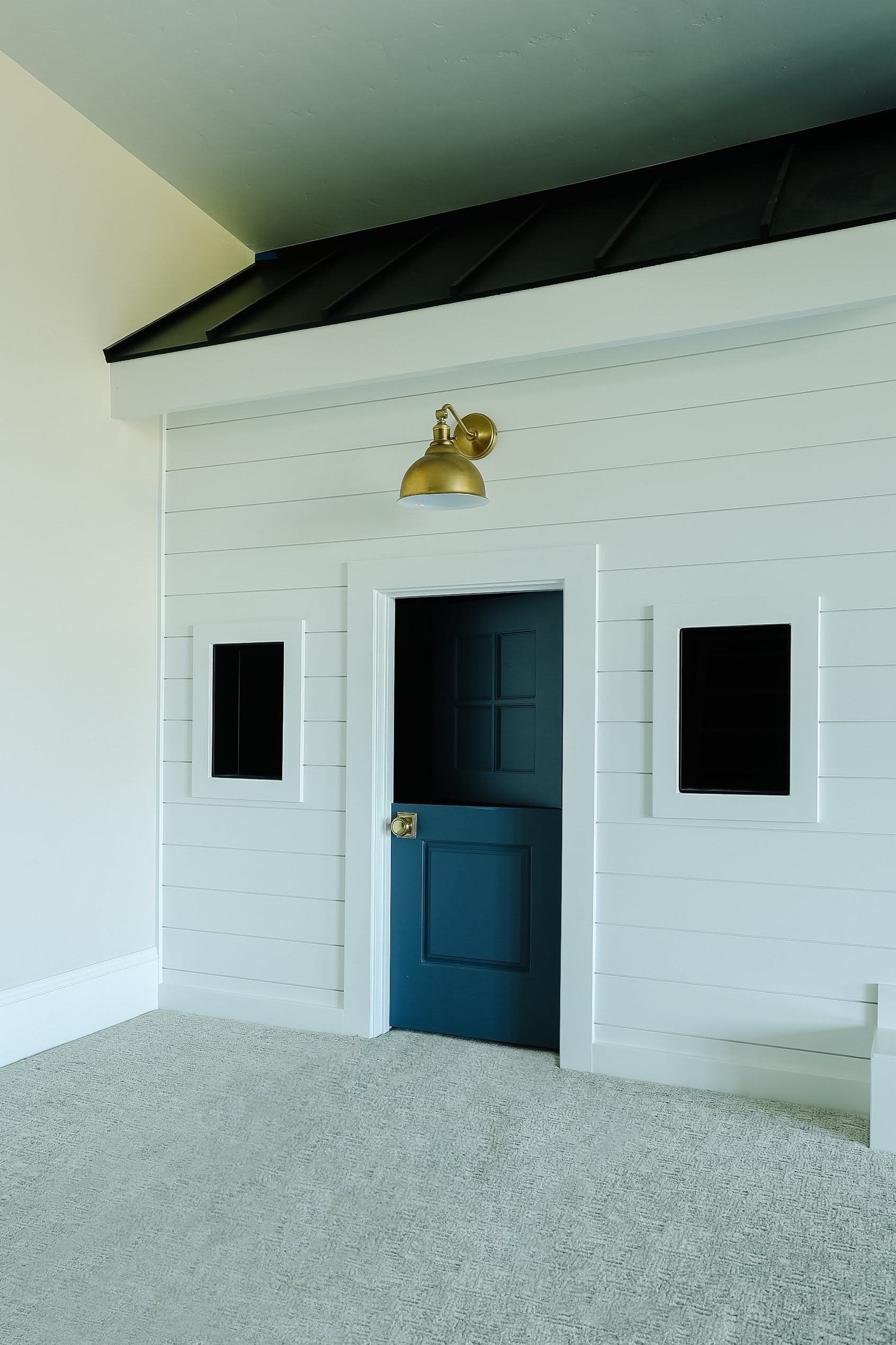 Parents of small children dream of a play area where their children’s imaginations will take them anywhere.&nbsp; Children’s play area Dutch door play house golden sconce light black and white #playarea #builtinplayhouse #shiplap #shingledplayhouse 