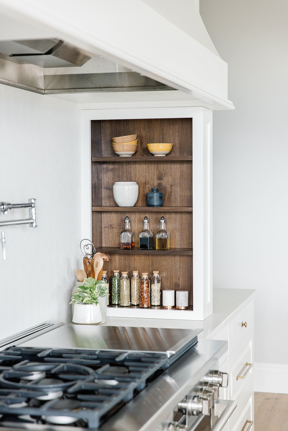  This kitchen uses the dead space of a wall to add built-in shelves next to the range. The wooden coloring is a perfect accent to the crisp white of the kitchen. Kitchen spice shelves dark walnut and white white kitchen #spiceshelves #woodandwhitekit