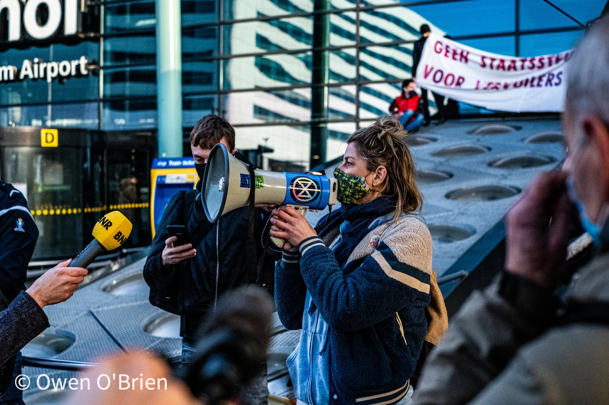 Een van de actievoerders van actiegroep Extinction Rebellion spreekt de toeschouwers toe die zich verzameld hebben op de luchthaven (december 2020).