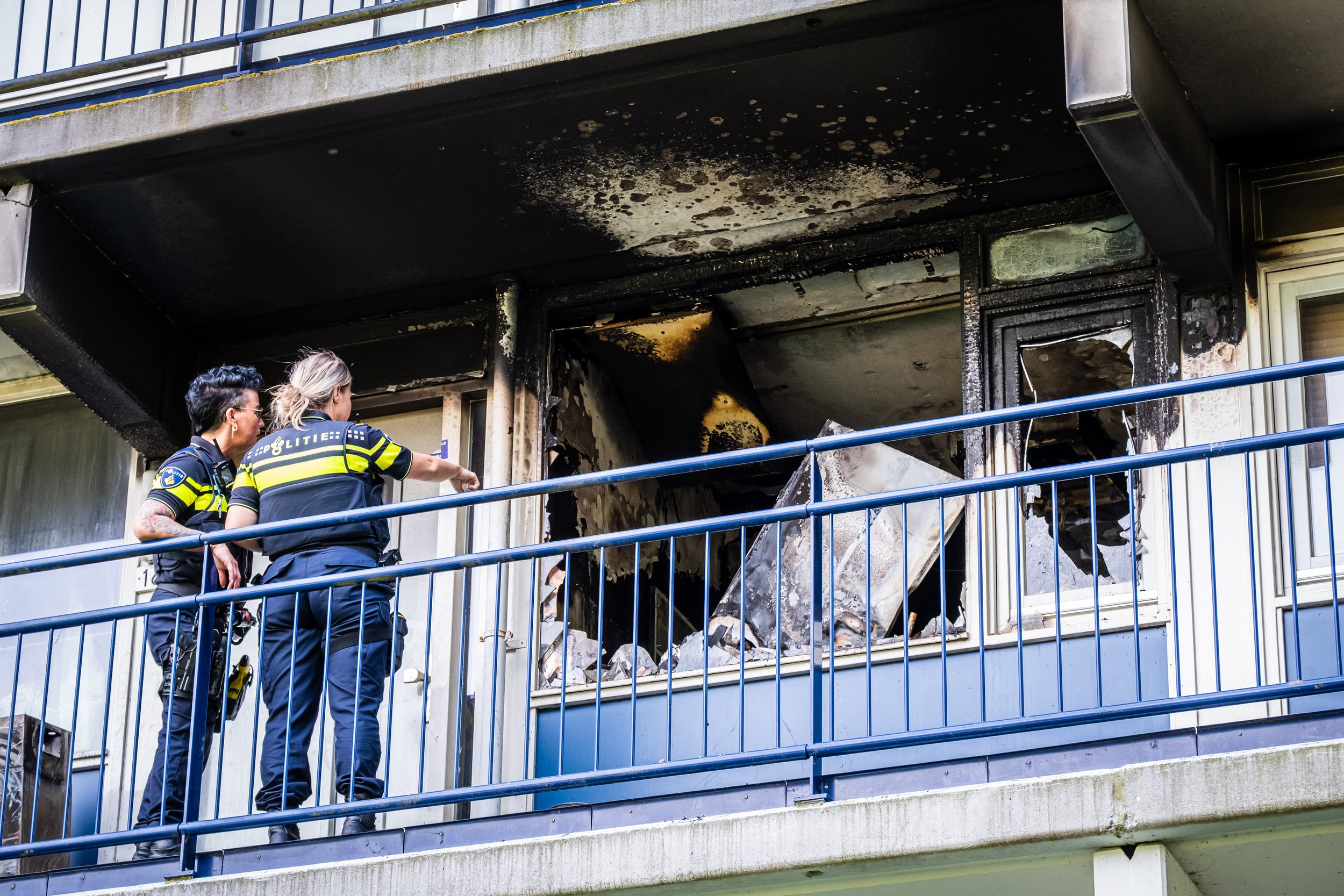 Een woning is onbewoonbaar als gevolg van brand in een flat in Leidschendam. Politieagenten bekijken de schade van dichtbij vanaf de galerij.