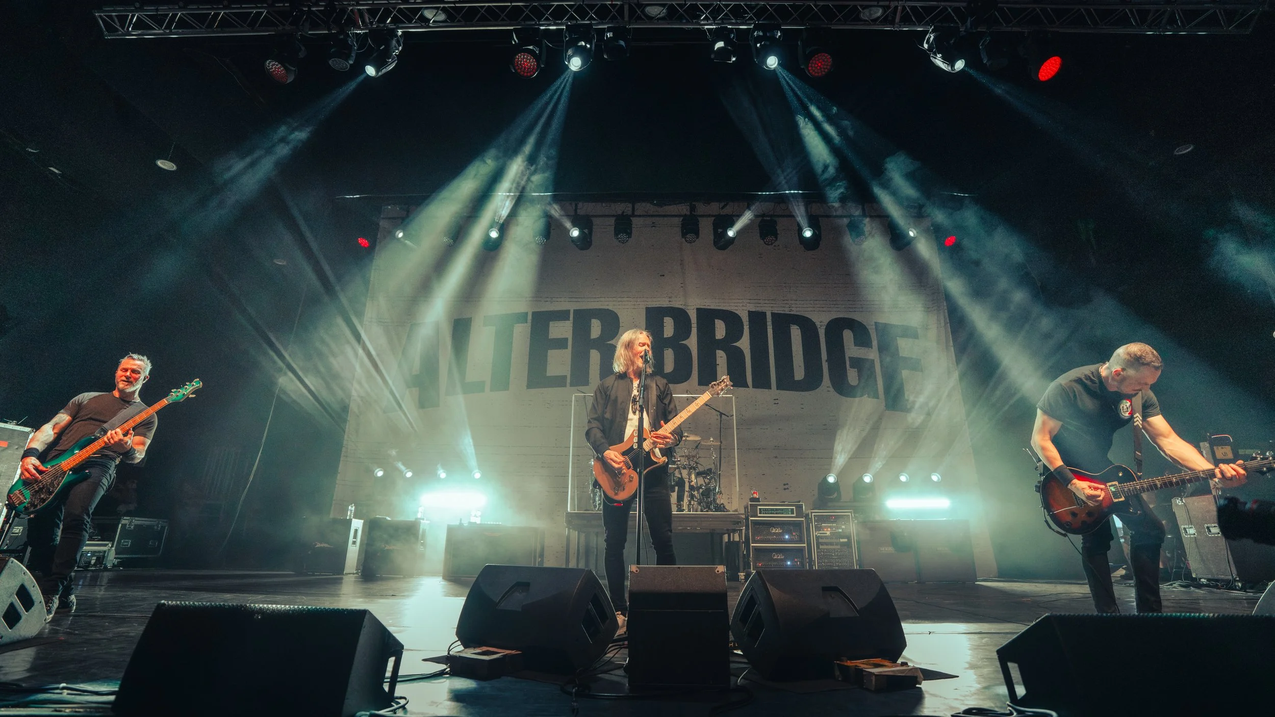 A band performing live on stage with large lights and smoke effects, and a backdrop with the words 'WATER BRIDGE'