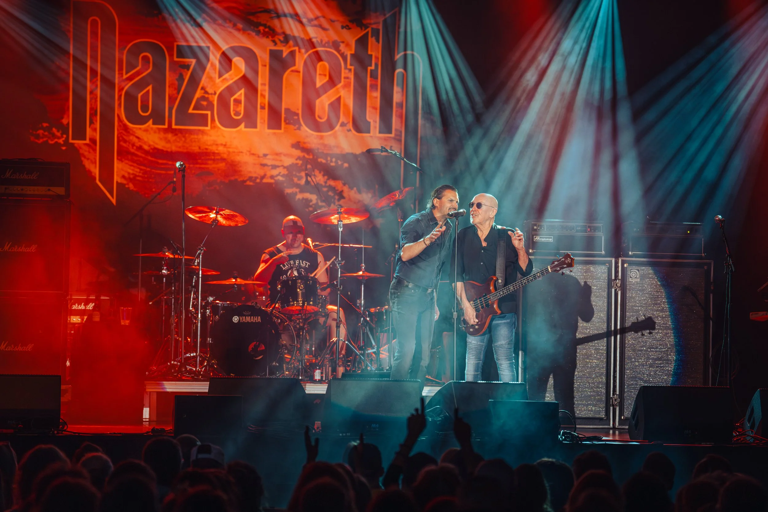 A live band performs on stage with bright colorful lighting and a backdrop with the word 'U2' in stylized font.