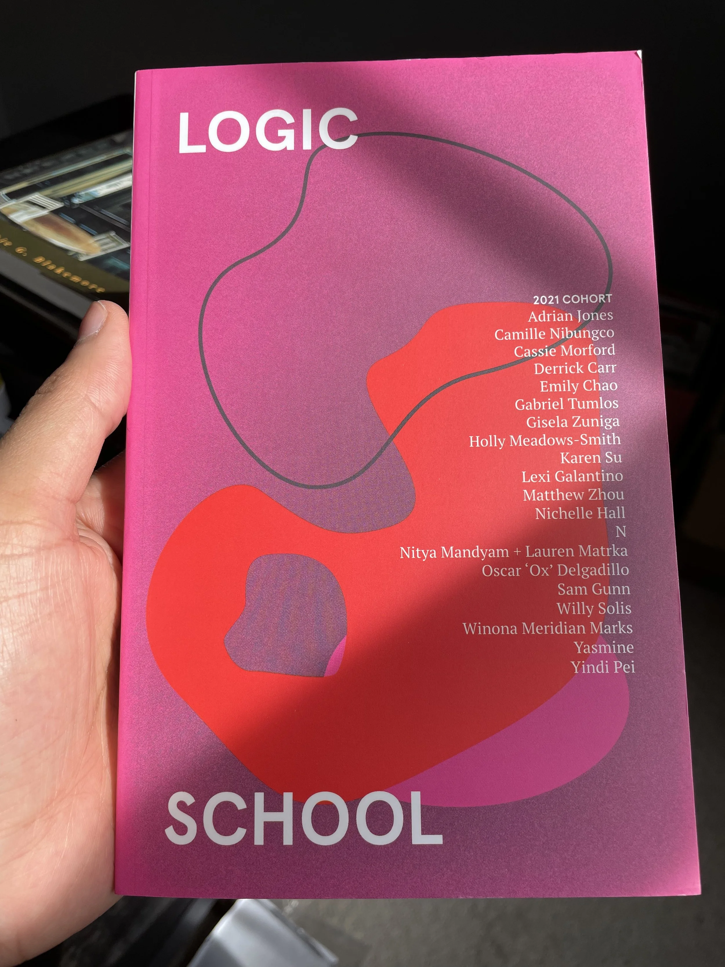 image of a hand holding a book that says "logic school". cover of the book is pink with purple pink gradients.