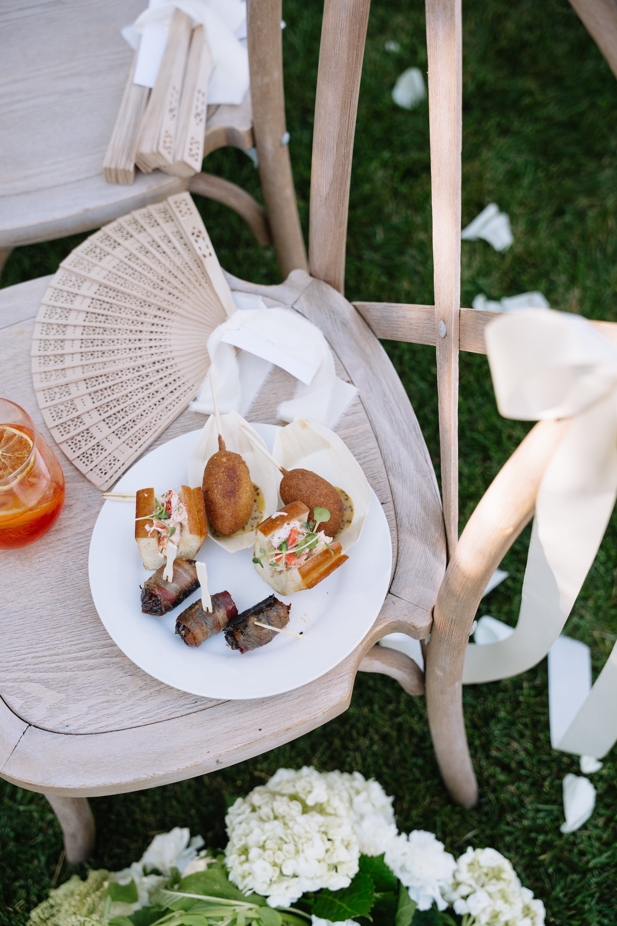 Plate of appetizers including corn dogs, bacon wrapped dates, and mini lobster rolls on a white plate