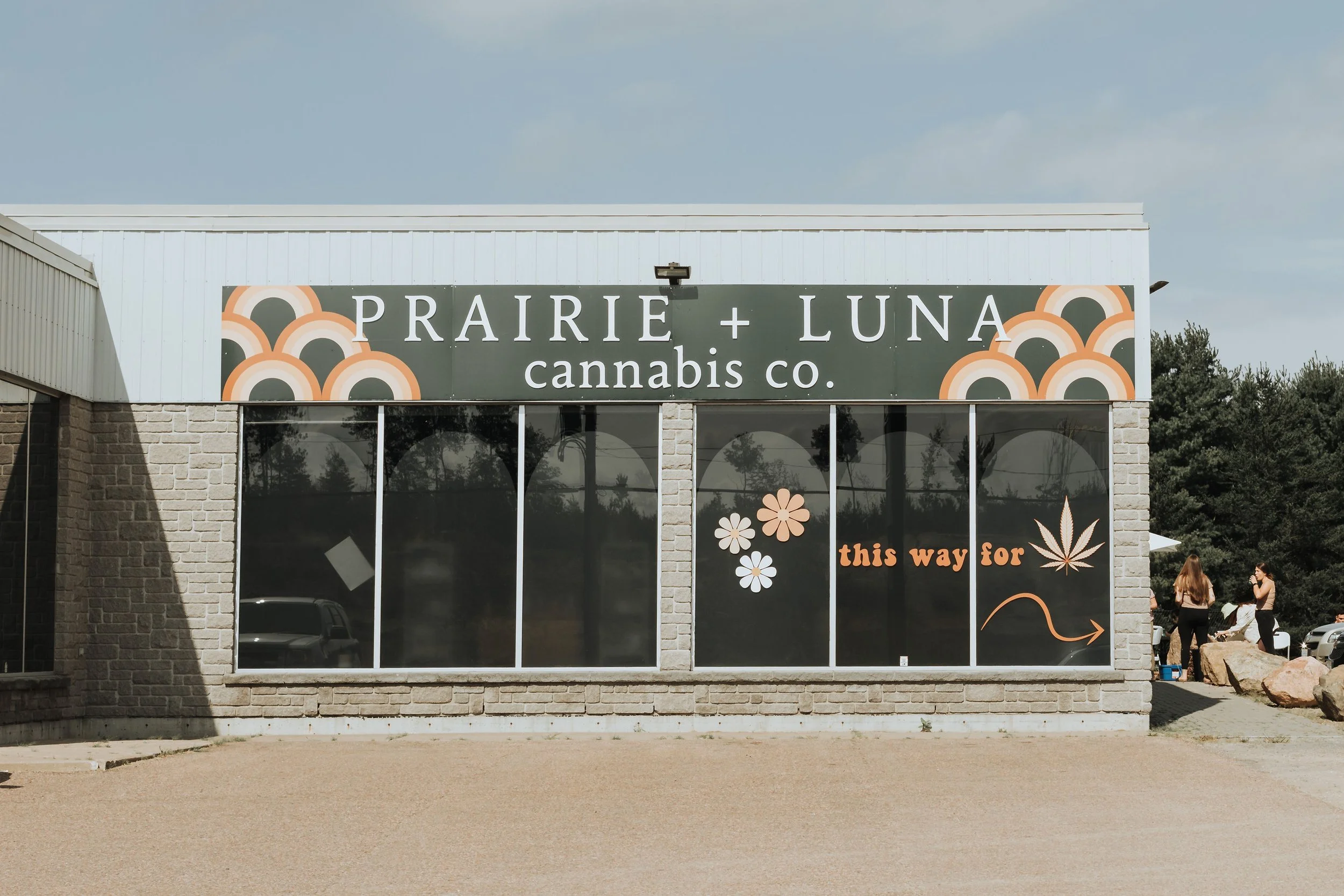 Prairie and Luna Cannabis Co. storefront with visible parking, signage reading “Cannabis This Way,” and cheerful brand icons like rainbows and smiley faces.