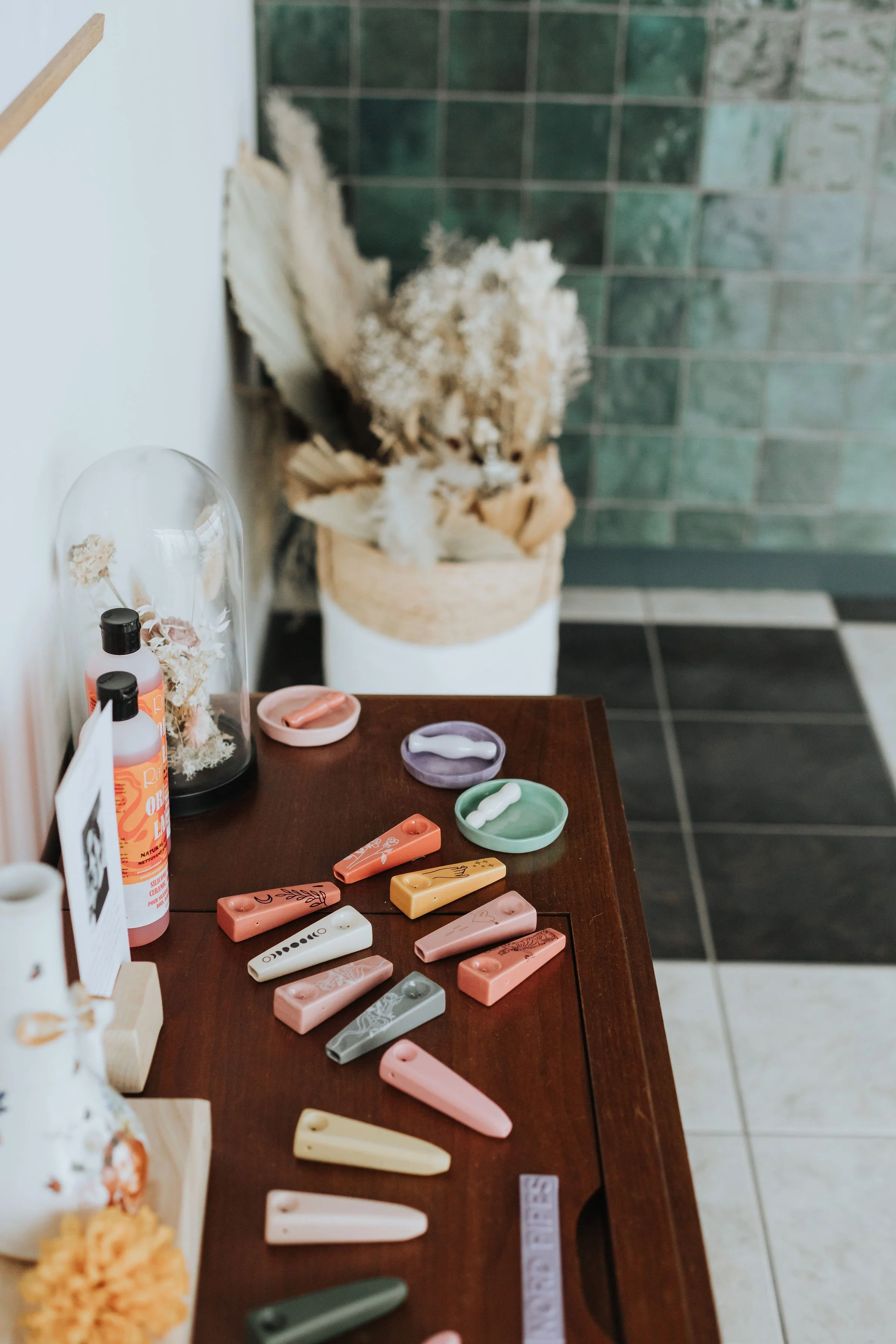 Handcrafted ceramic pipes and stash dishes on a wooden table, with dried florals and green tile backdrop inside Prairie and Luna.