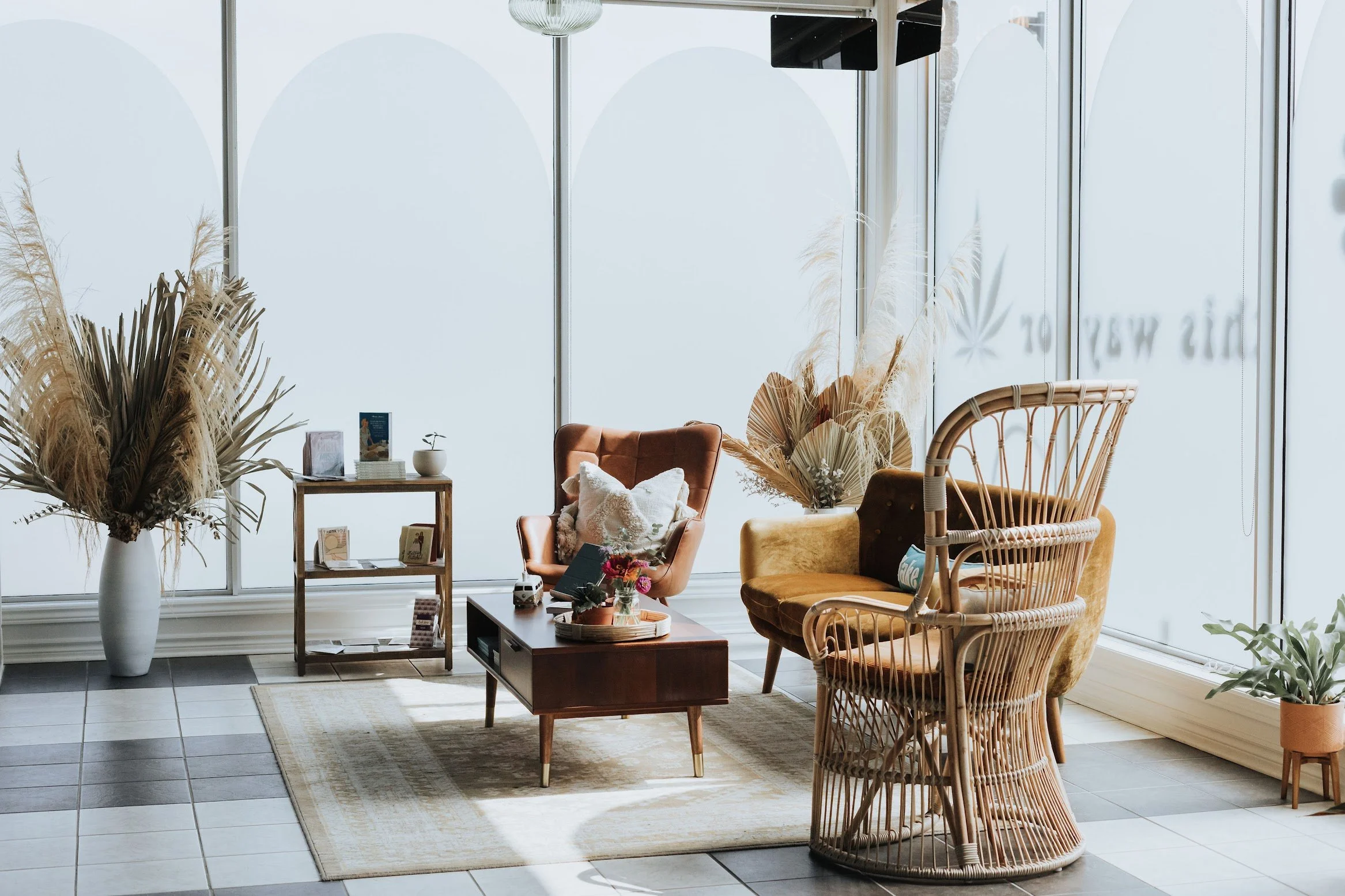 Inviting lounge corner with rattan and velvet seating, wooden coffee table, dried florals, and floor-to-ceiling windows streaming natural light.