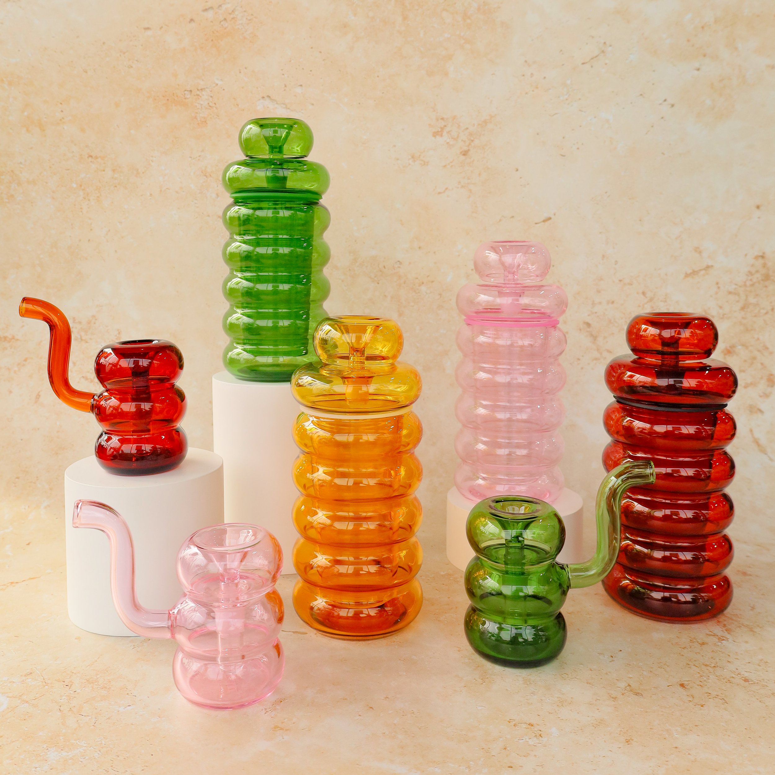 NWTN Deco ribbed borosilicate glass gravity bongs and bubblers displayed on pedestals in emerald green, amber gold, rose pink, and honey yellow colour ways at Prairie and Luna.