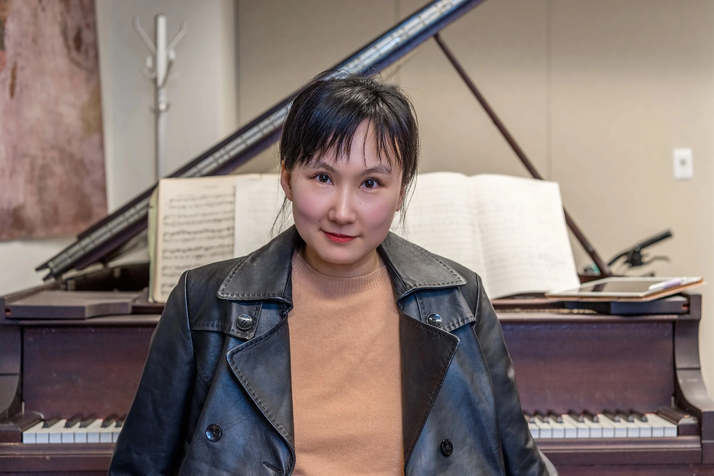Asian woman sitting in front of piano with music score behind her.