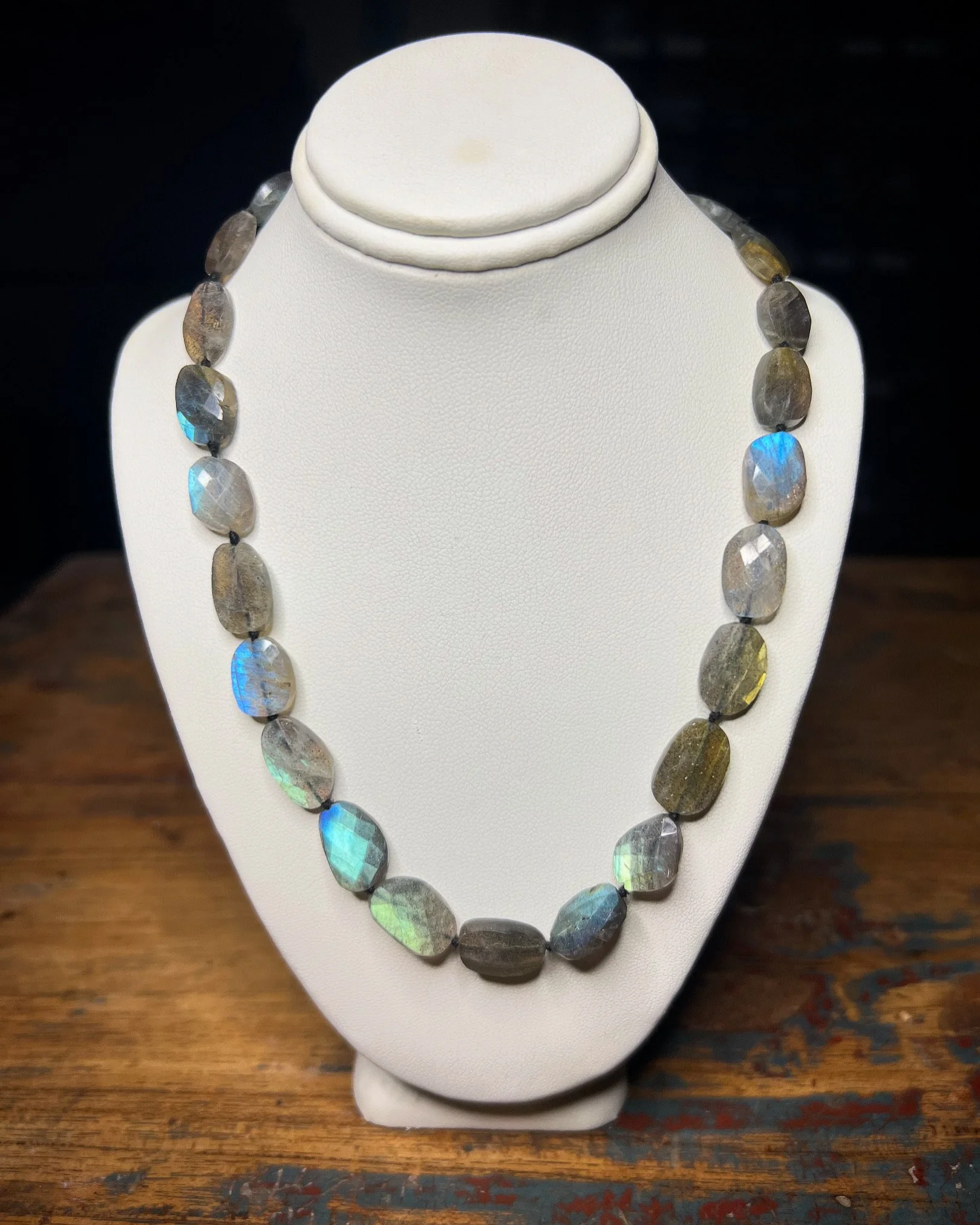 Labradorite gemstone necklace displayed on a white jewelry bust, sitting on a wooden surface.