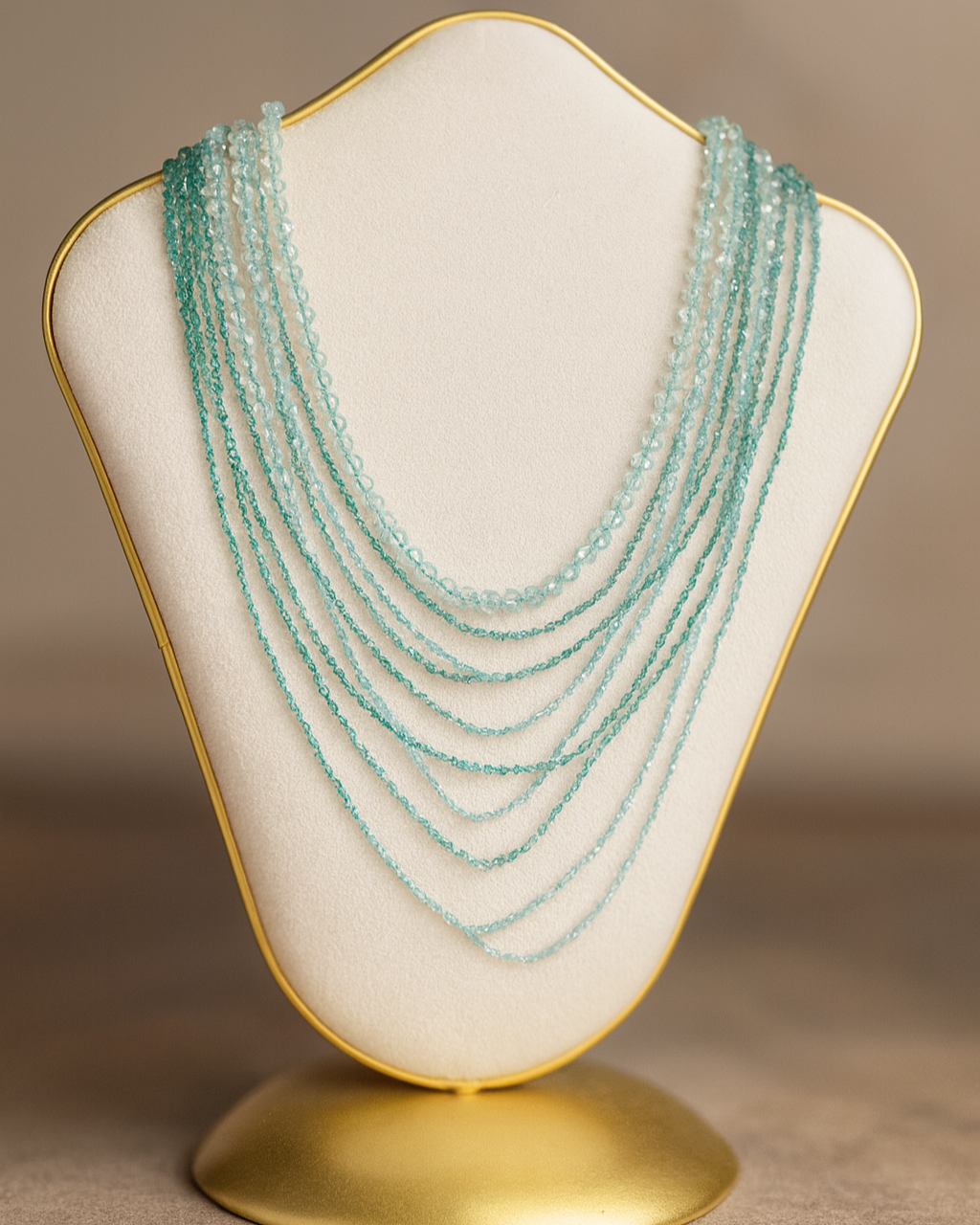 Multiple strands of light blue beads displayed on a beige jewelry stand with a gold outline.