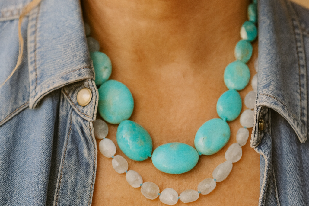 Close-up of a woman’s neck and lower face, wearing multiple turquoise and white beaded necklaces, and a denim shirt.