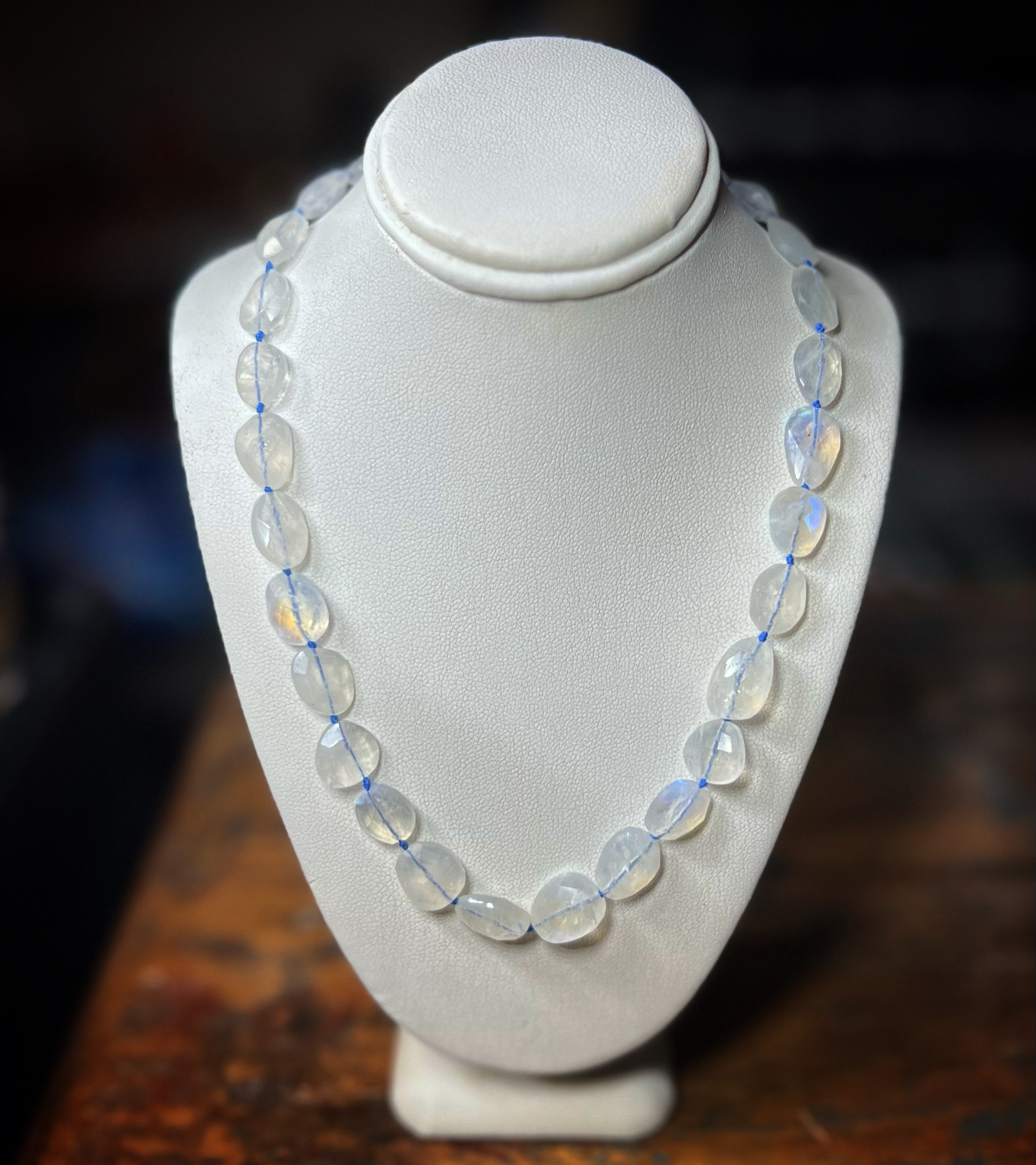 Necklace made of rainbow moonstone, oval-shaped beads displayed on a white jewelry bust.