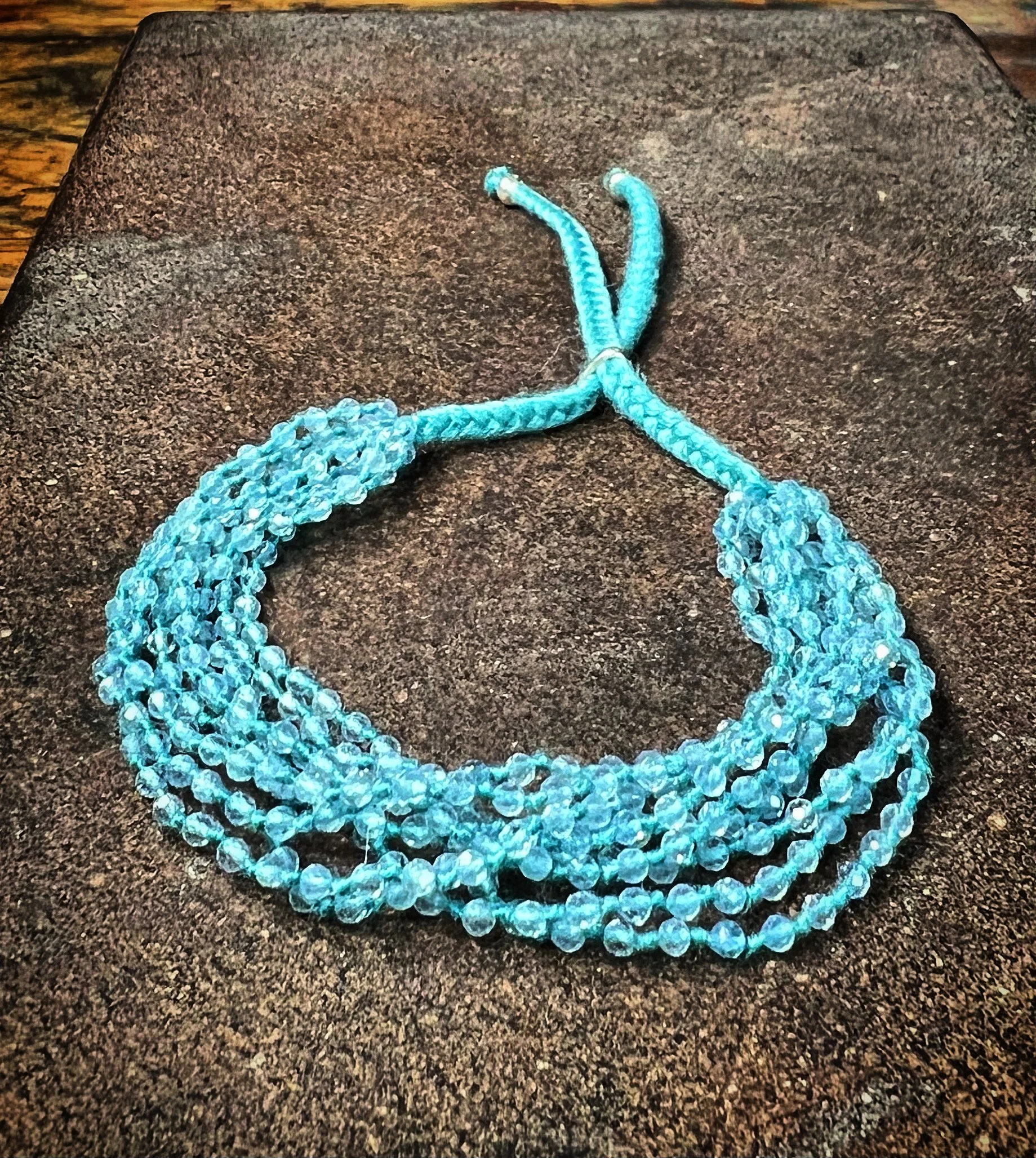 An aquamarine bracelet with multiple strands, resting on a dark textured surface.