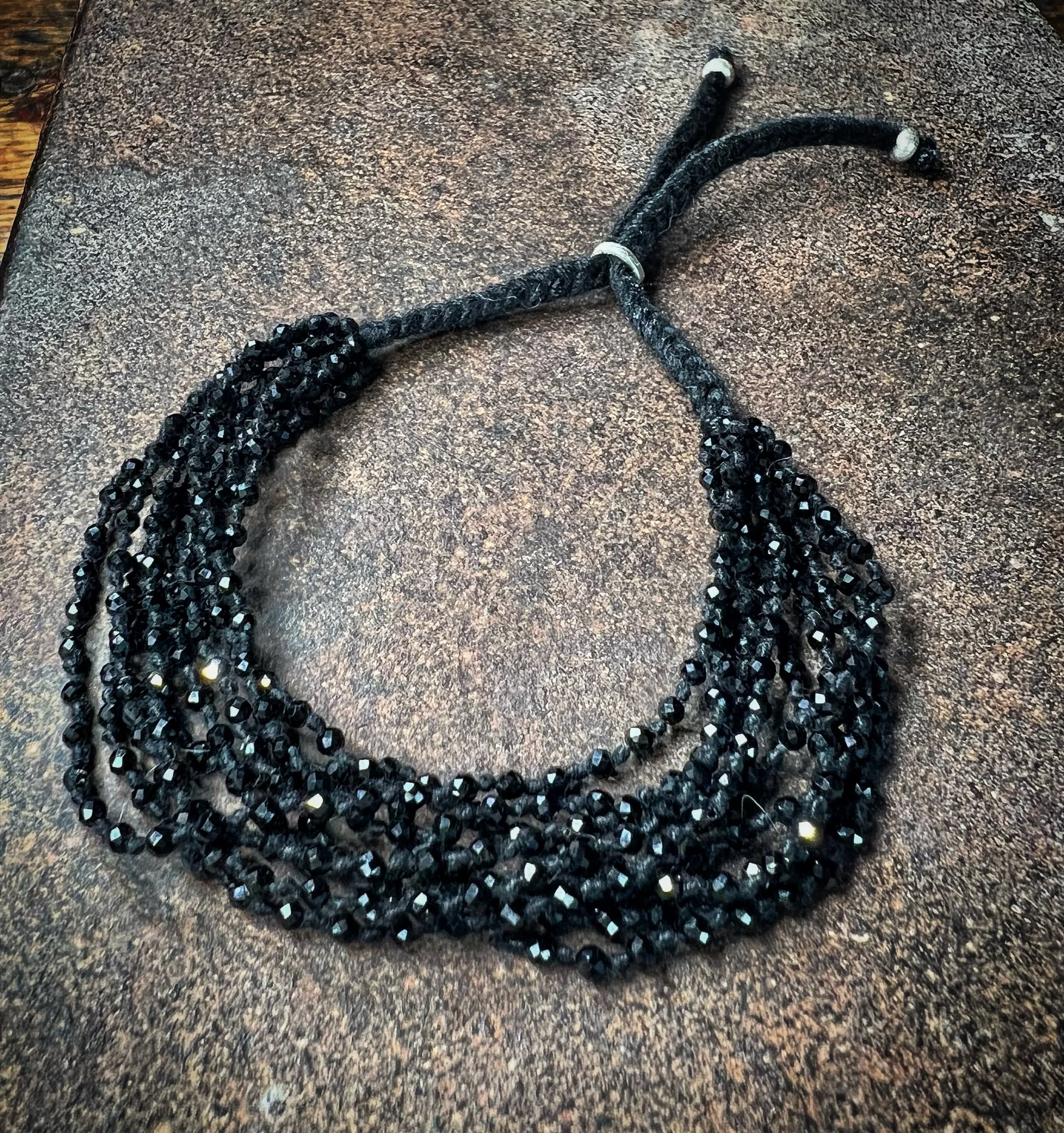 Black spinel bracelet with a braided black cord on a textured brown surface.