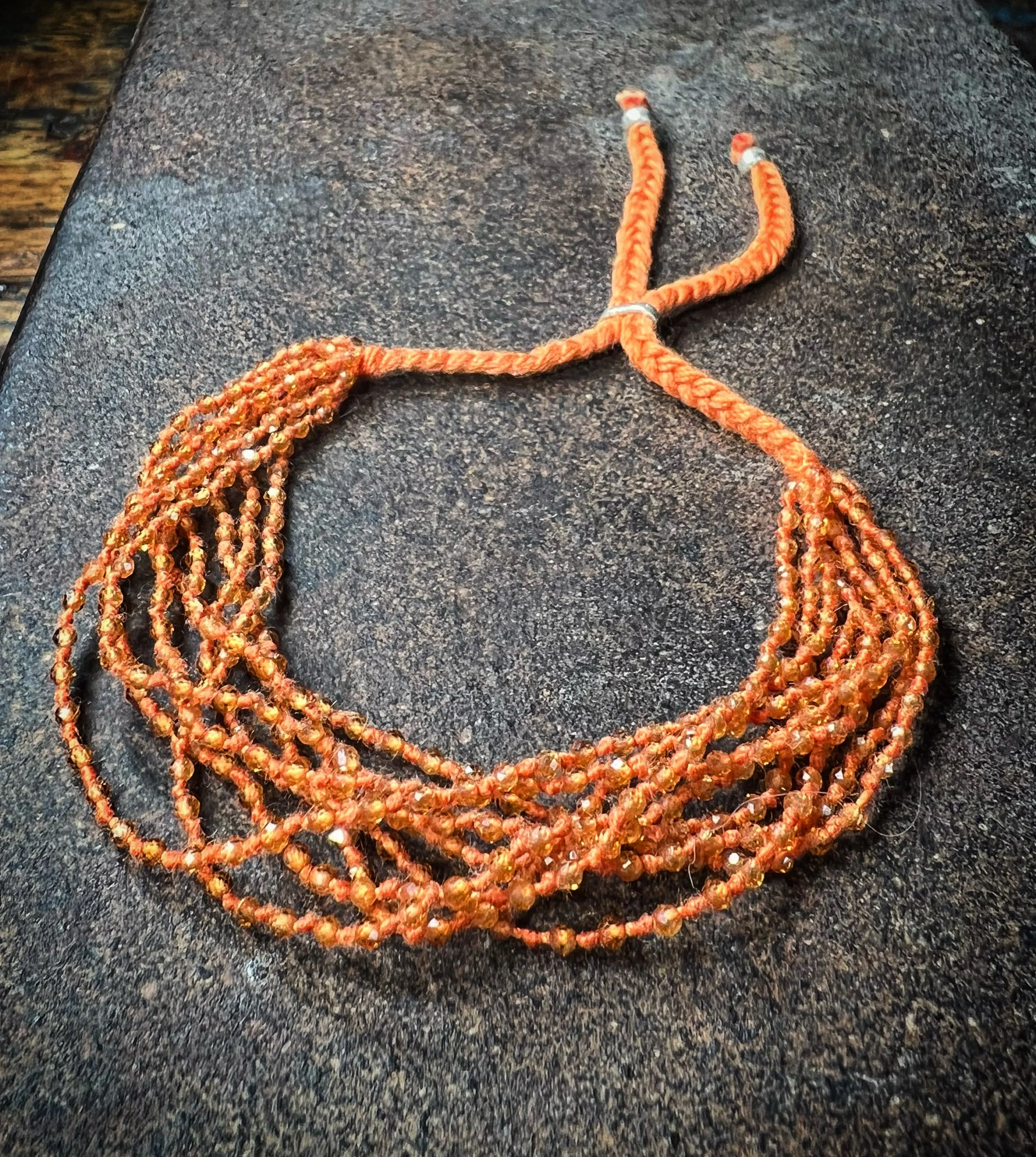 An orange sapphire bracelet with multiple strands and a braided cord, displayed on a dark surface.