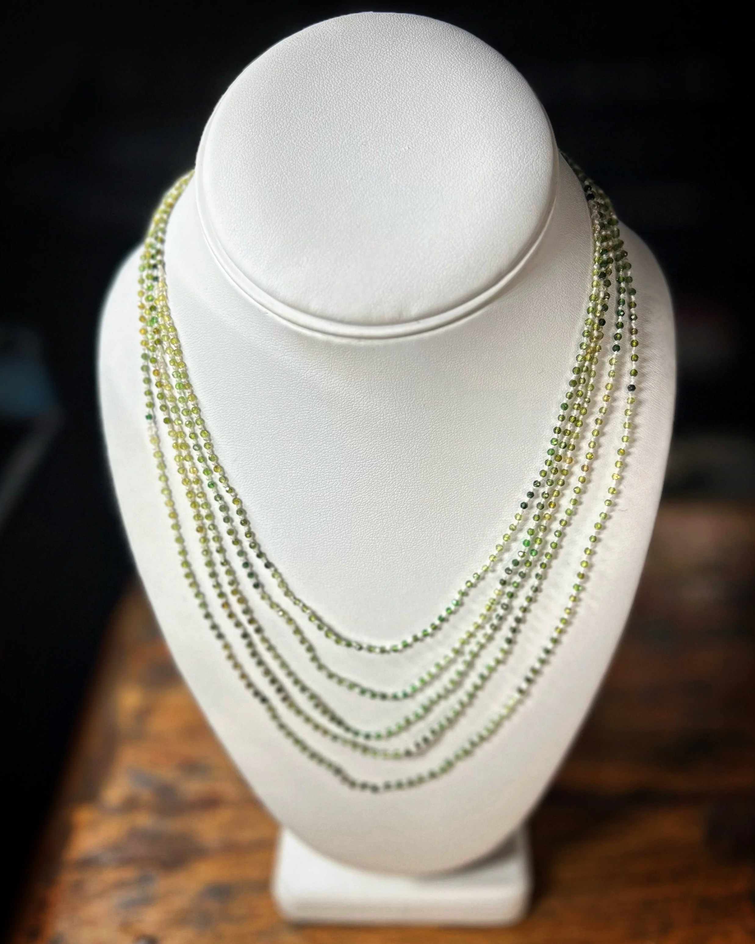 Necklace display with multiple layered strands of green tourmaline on a white mannequin bust.