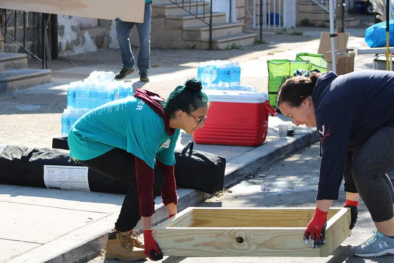 Two volunteers work together to lift up a wooden box from the ground.