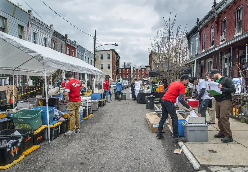 On the streets of Philly, volunteers at a Block Build look through supplies in boxes under tents.