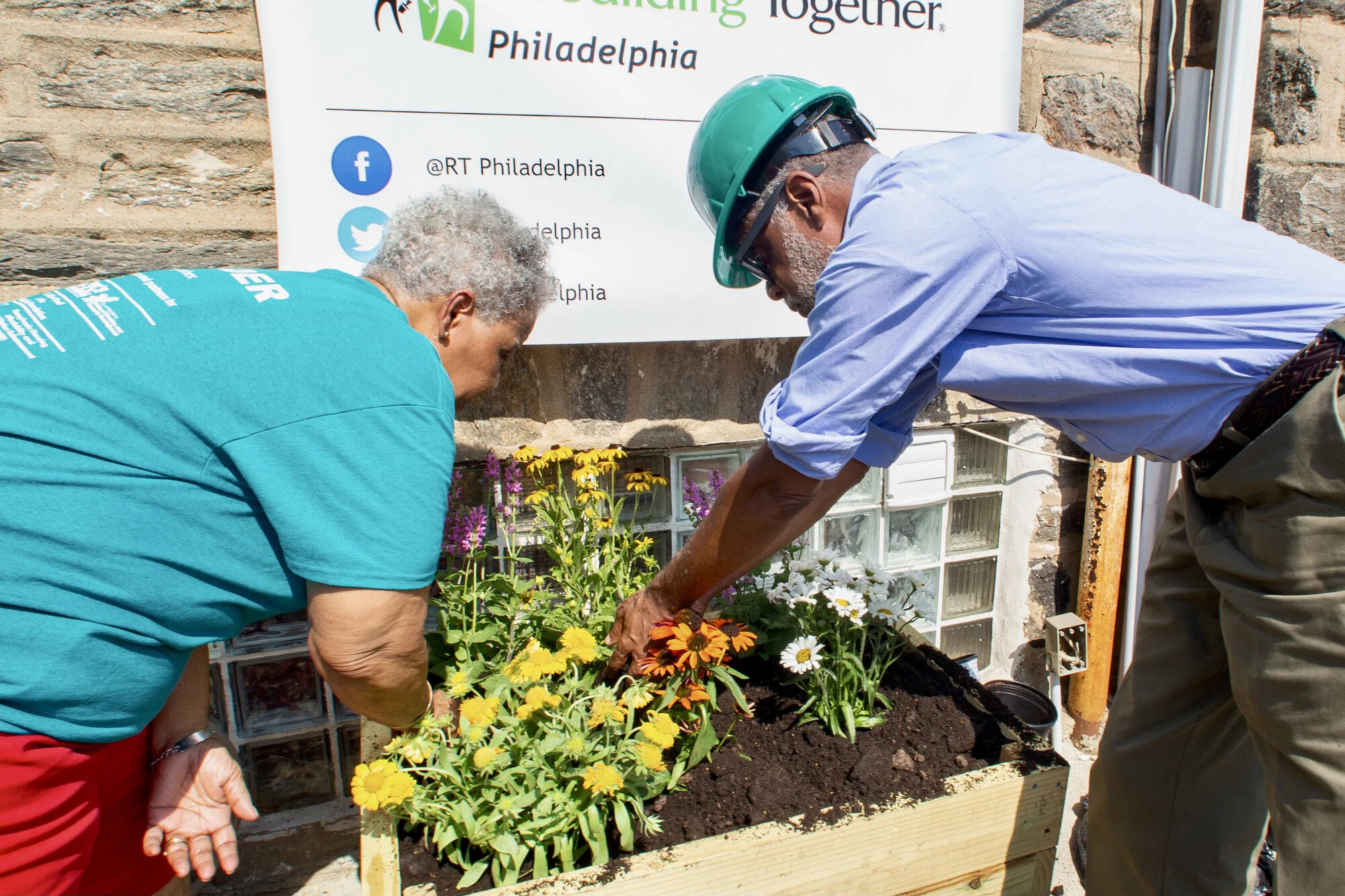The volunteers are planting flowers in a garden bed as part of a community beautification project.
