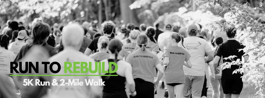 A black and white picture of runners wearing shirts with the words Run to Rebuild seen from behind