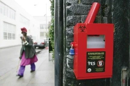 Red biohazard disposal box attached to a black wall with a biohazard symbol on it