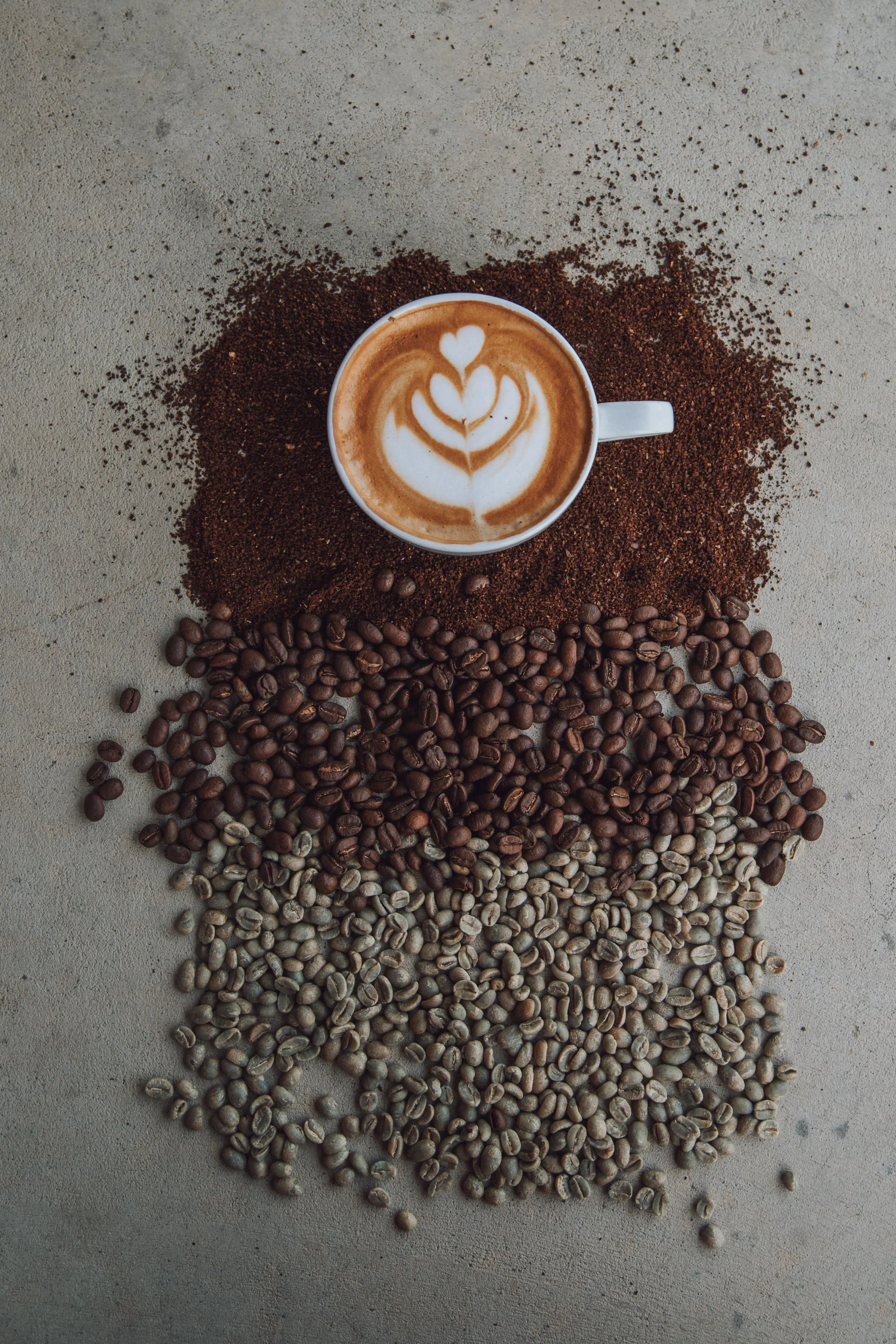 A coffee cup with latte art surrounded by coffee grounds and coffee beans.