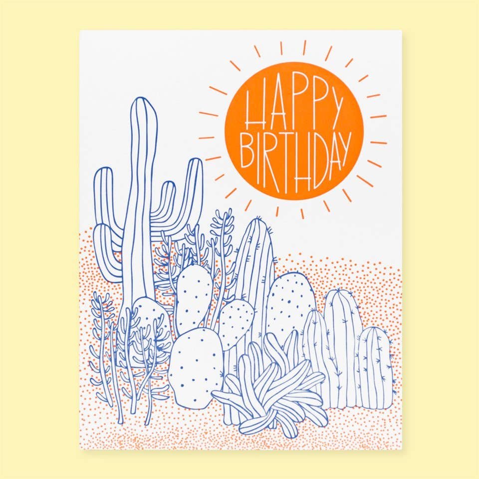 Image of Greeting Card With A Hand-Drawn Desert Scene. Blue Line-Drawn Cacti Garden On Pinkish-Orange Dotty Sand And “Happy BIrthday” In Hand-Drawn Type On A Bold Orange Sun Upper Right Corner