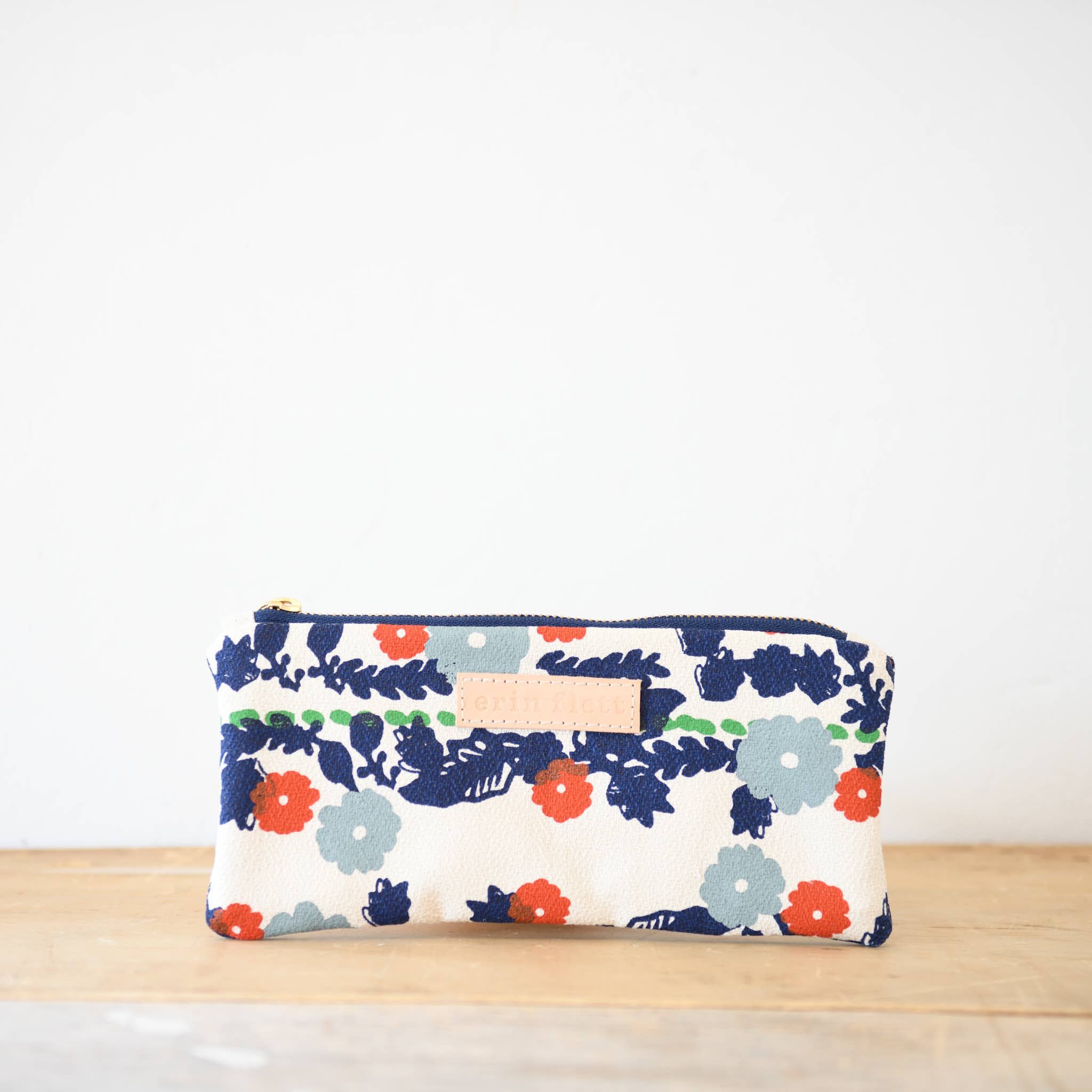 Image Of Floral Natural Canvas Pencil Bag With Navy, Mint Blue, Green And Red Floral Design. There Is A Leather Designer Name Tag On The Side And A Zipper Closure.
