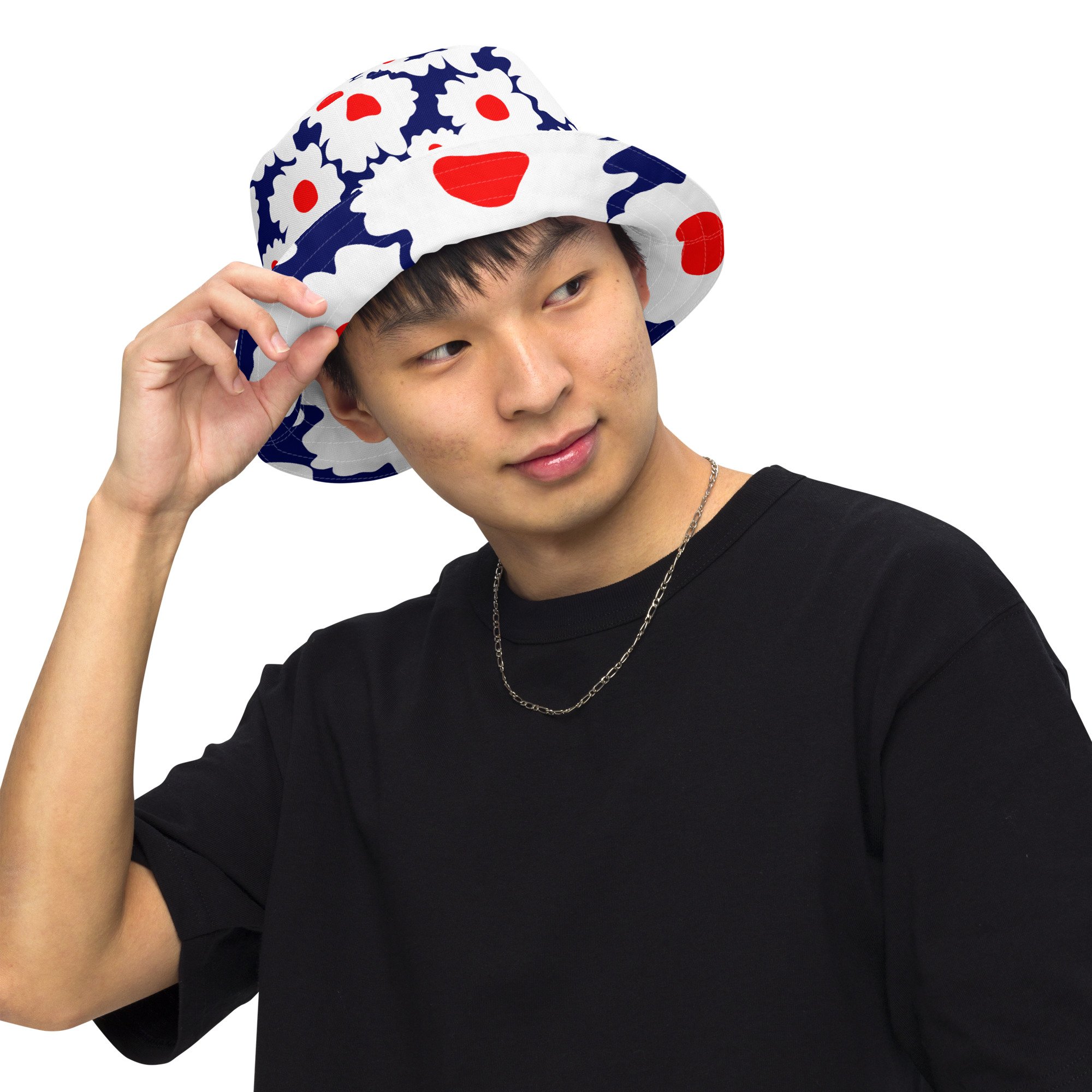 Image of Young Man Wearing A Reversible Bucket Hat With Big Red, White And Blue Abstract Flowers Pattern. One Side Has A Big Floral Pattern, The Other Has A Smaller Flower Print.
