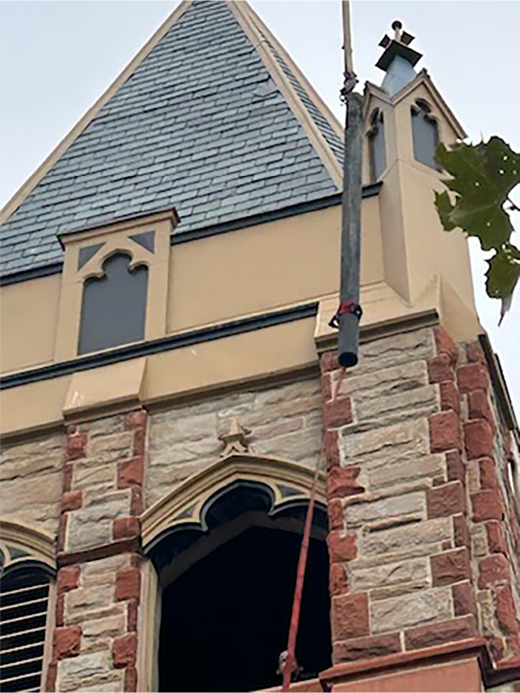 Primer plano del campanario de una iglesia histórica de piedra con un cable de grúa durante un proyecto de restauración de un carillón tubular Deagan llevado a cabo por Chime Master.