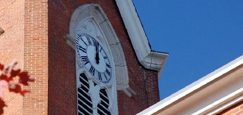 Reloj tradicional de torre de iglesia instalado en un campanario de ladrillo con un cielo azul de fondo