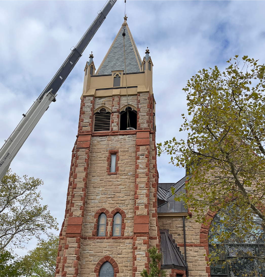 Campanario histórico de una iglesia y tejado de pizarra con aguja, con el equipo de grúa instalado durante un proyecto de instalación y restauración de un carillón tubular Deagan a cargo de Chime Master.