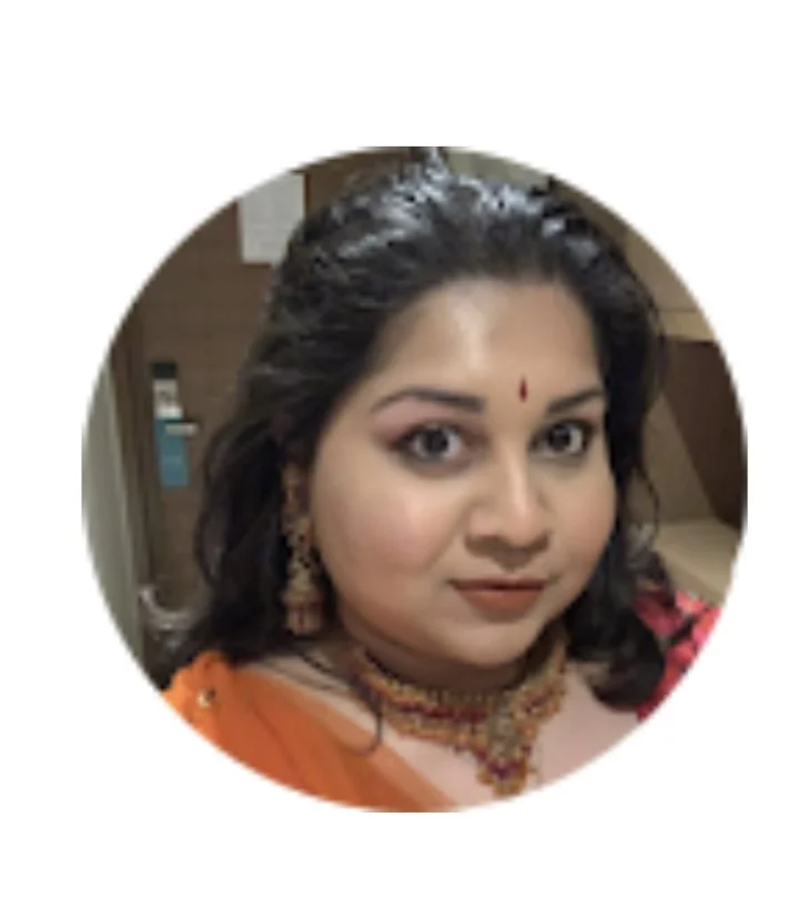 A woman with dark hair wearing traditional Indian jewelry and clothing, with a red bindi on her forehead.