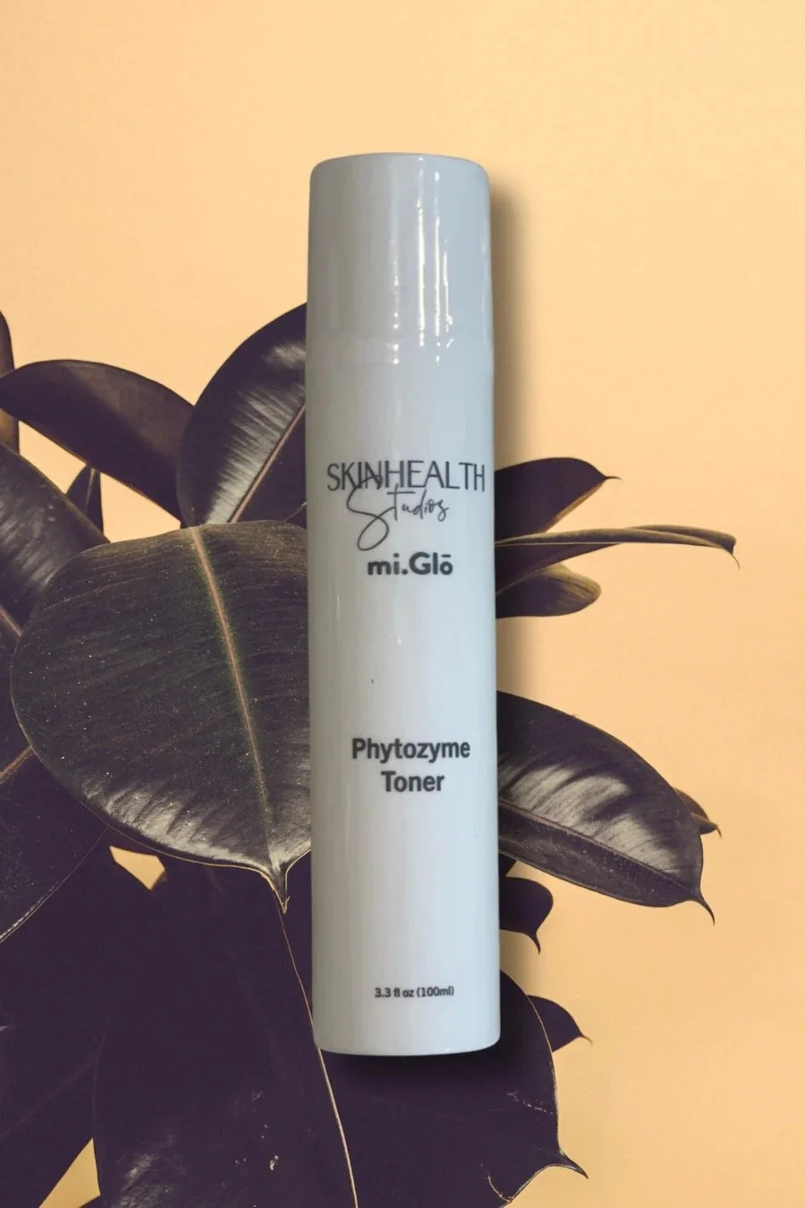 A white bottle labeled Skin Health Studios Mi.Glo Phytozyme Toner, standing against dark green leaves and a light yellow background.