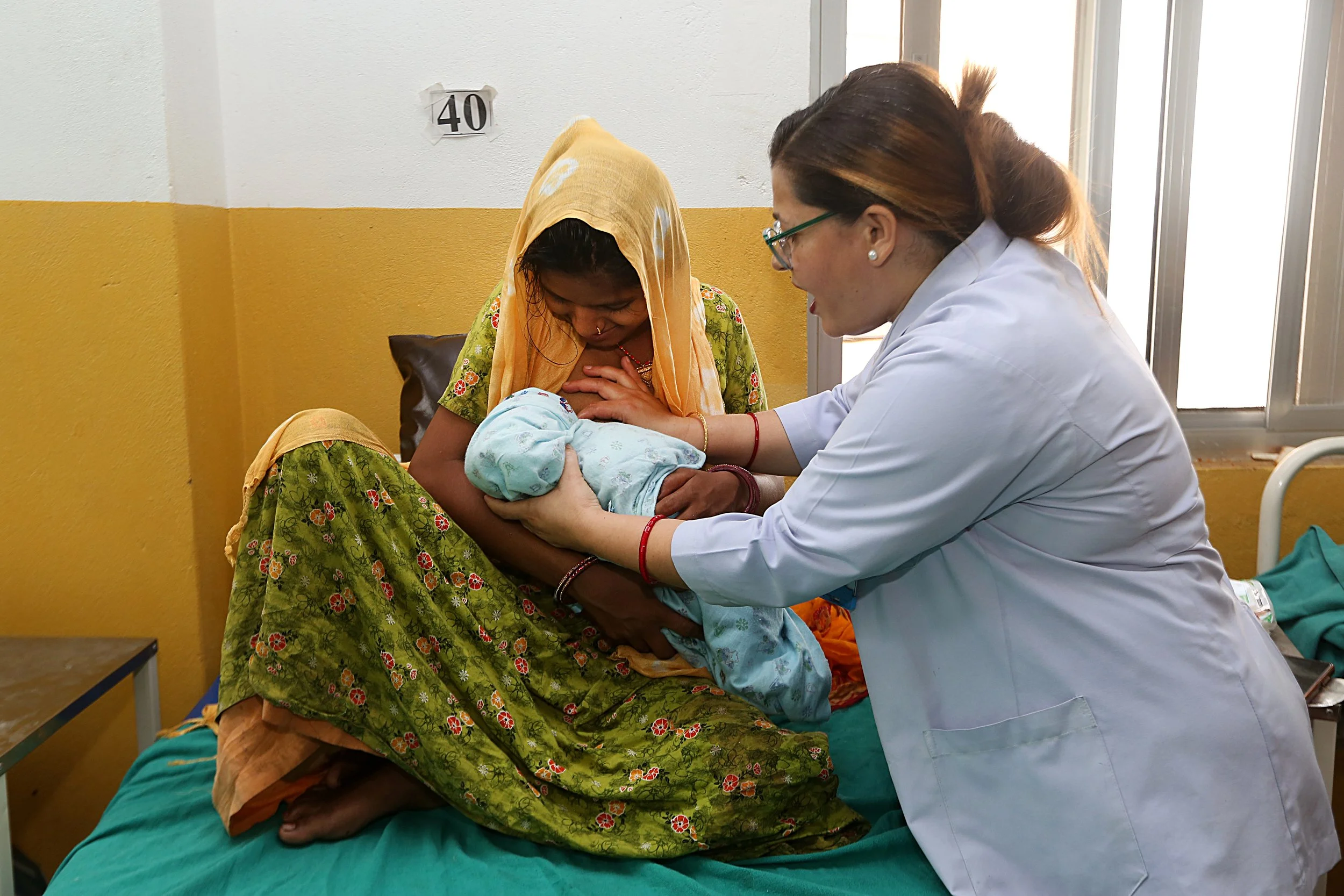 A skilled birth attendant in Nepal helps a new mother position her newborn for breastfeeding at a health facility.