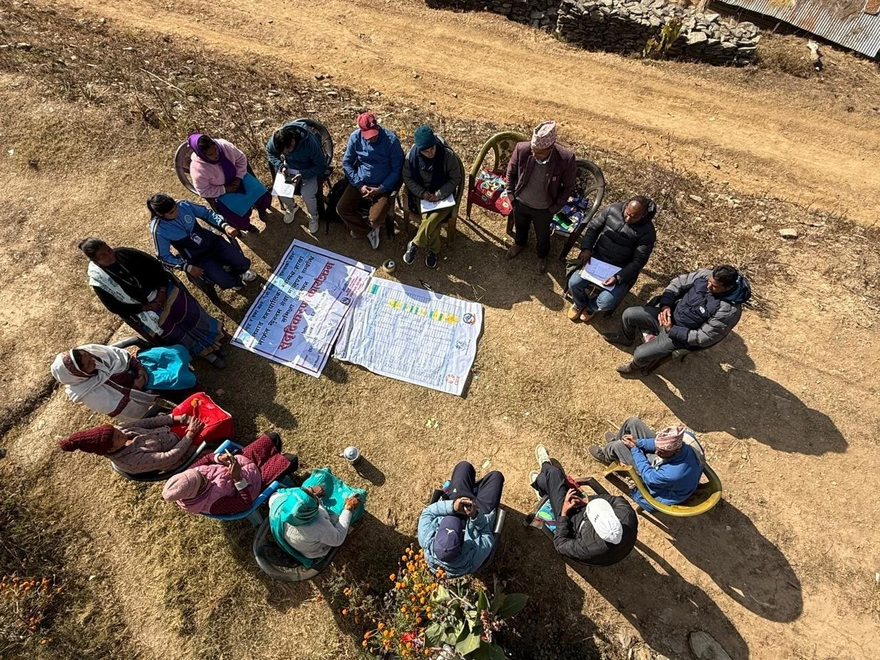 Overhead view of a quality improvement discussion at Lanha health post in Nepal, with participants seated in a circle around program charts.