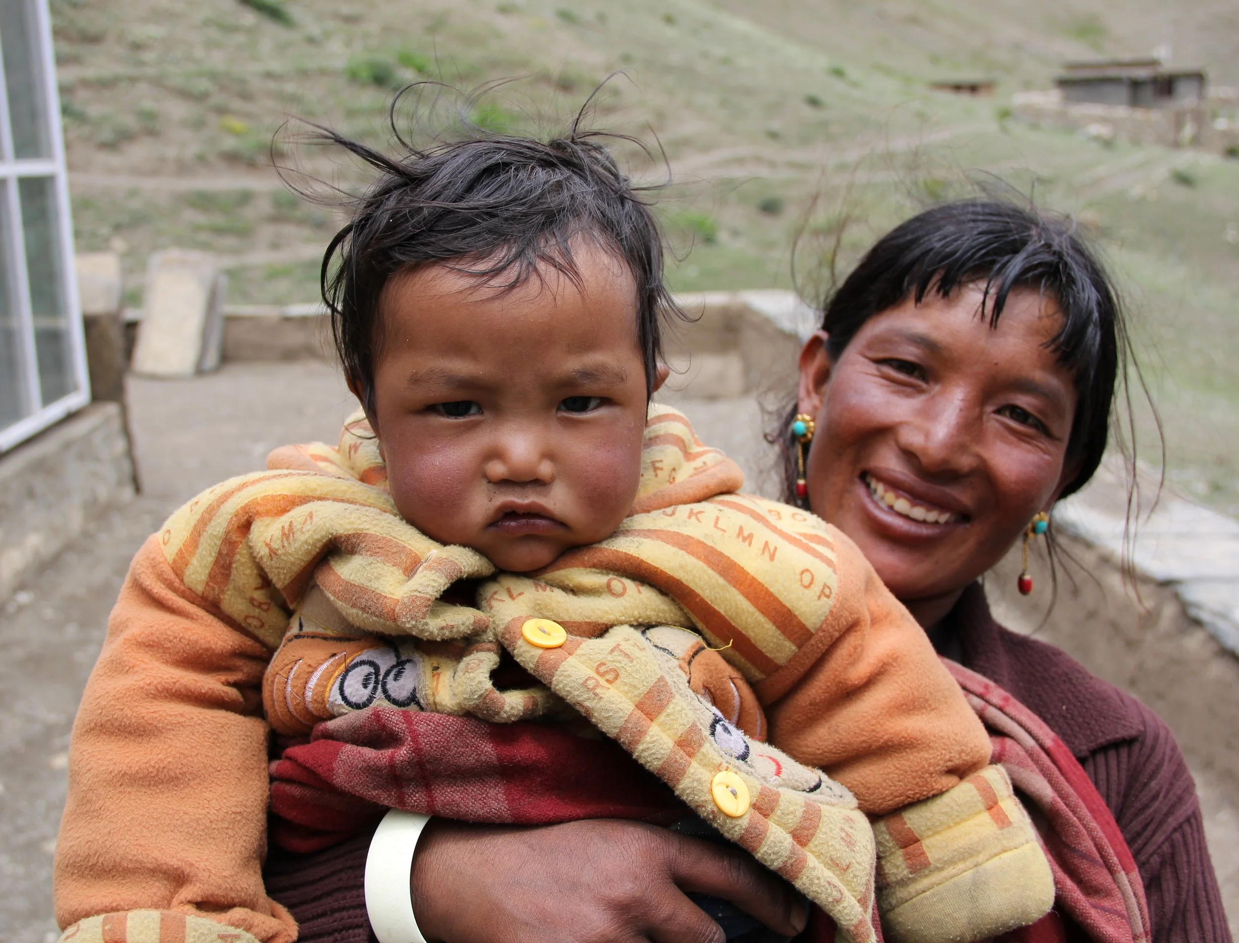 A smiling mother holding up her baby for the camera in the mountains of Nepal.