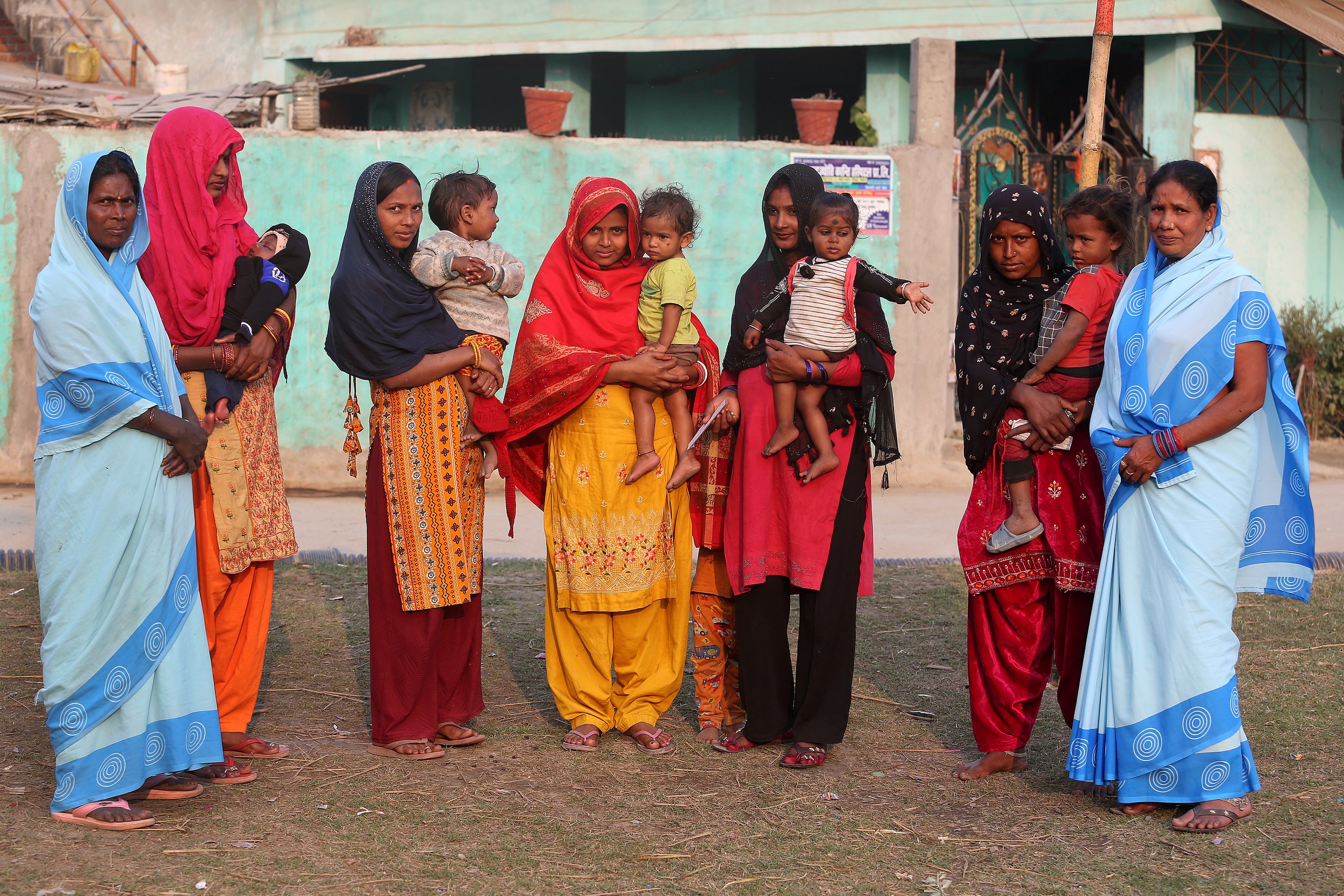 Mothers stand together holding their young children outside a health facility after a community awareness event.