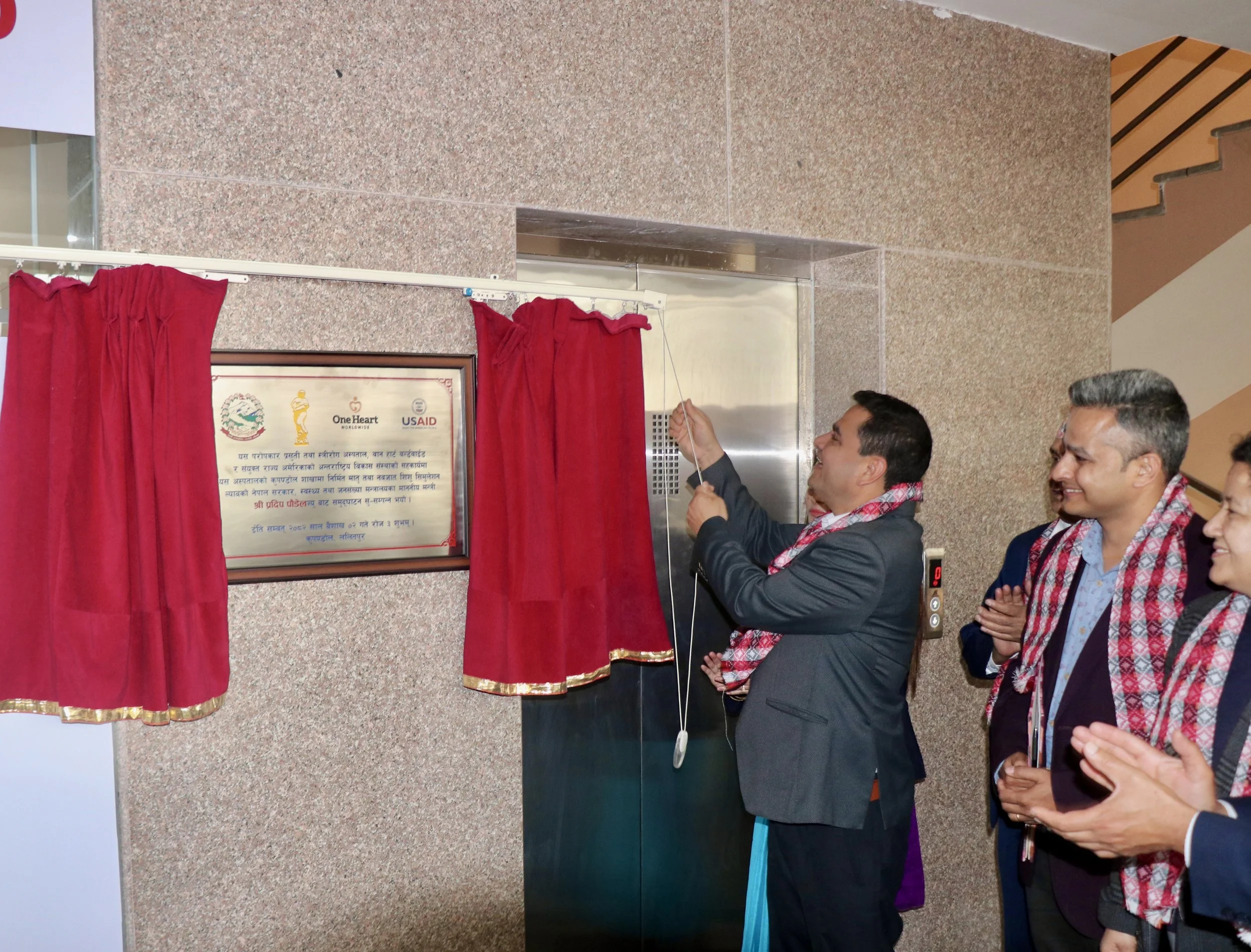 Officials unveil a plaque marking a health facility built in partnership with the Government of Nepal, One Heart Worldwide, and USAID, as onlookers applaud.