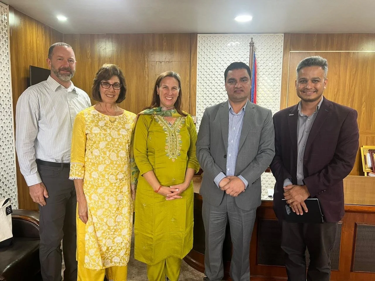 One Heart Worldwide and government partners stand together at a meeting in Nepal, with the national flag behind them.