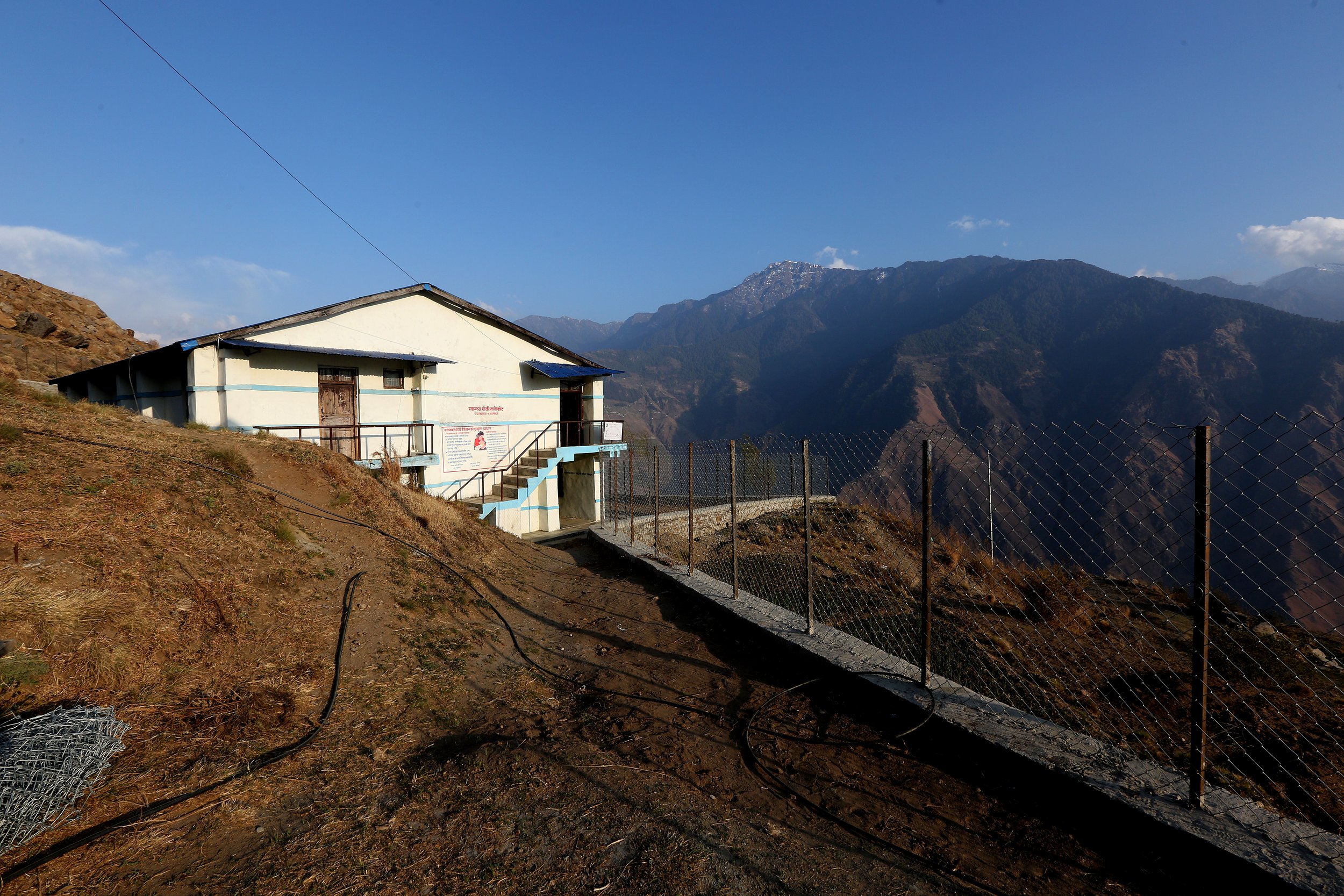 A health post sits on a mountain ridge in Nepal, overlooking a deep valley.