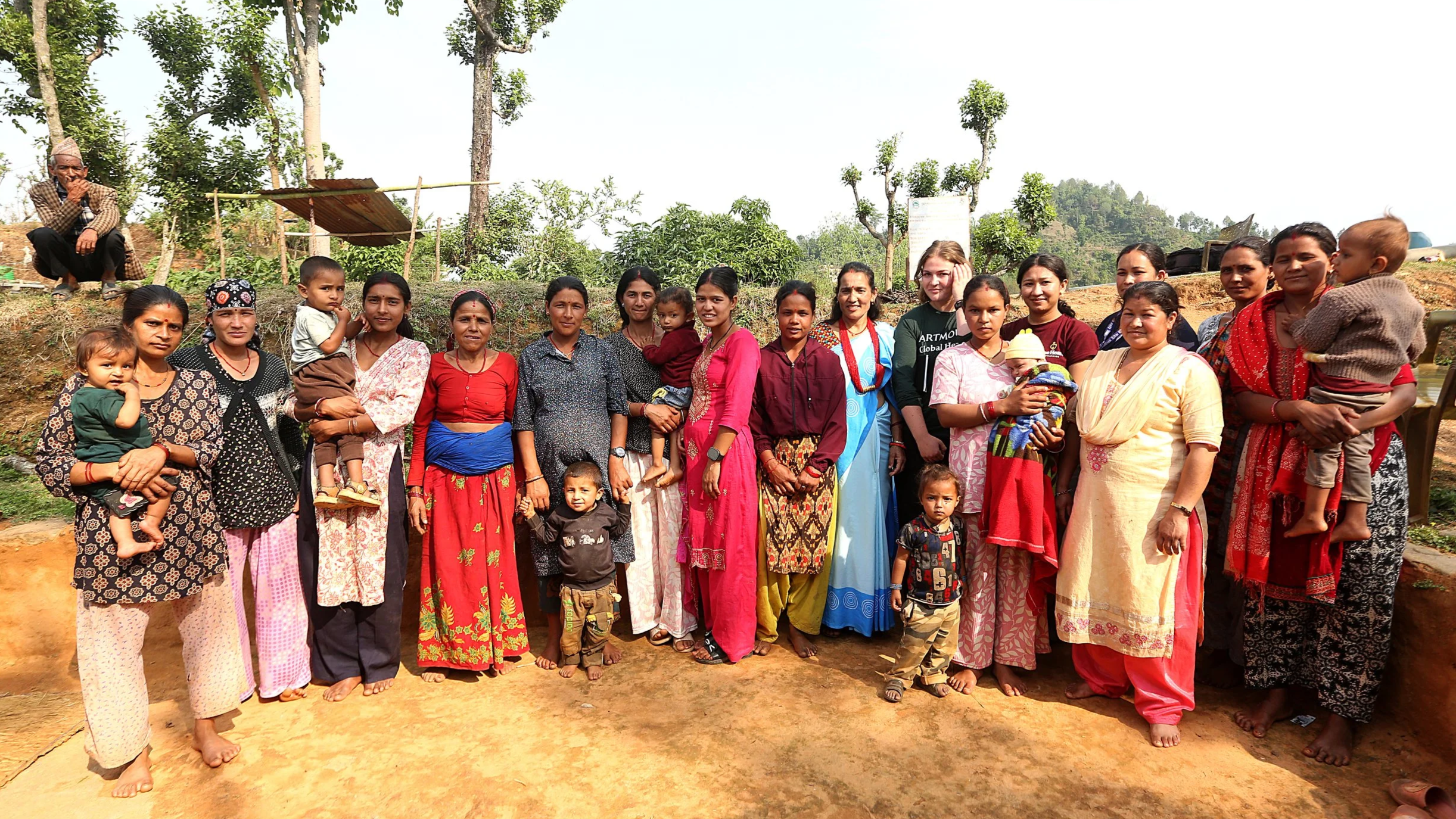 A large group of mothers and their children gather with a community health team outside in a hillside village in Nepal.