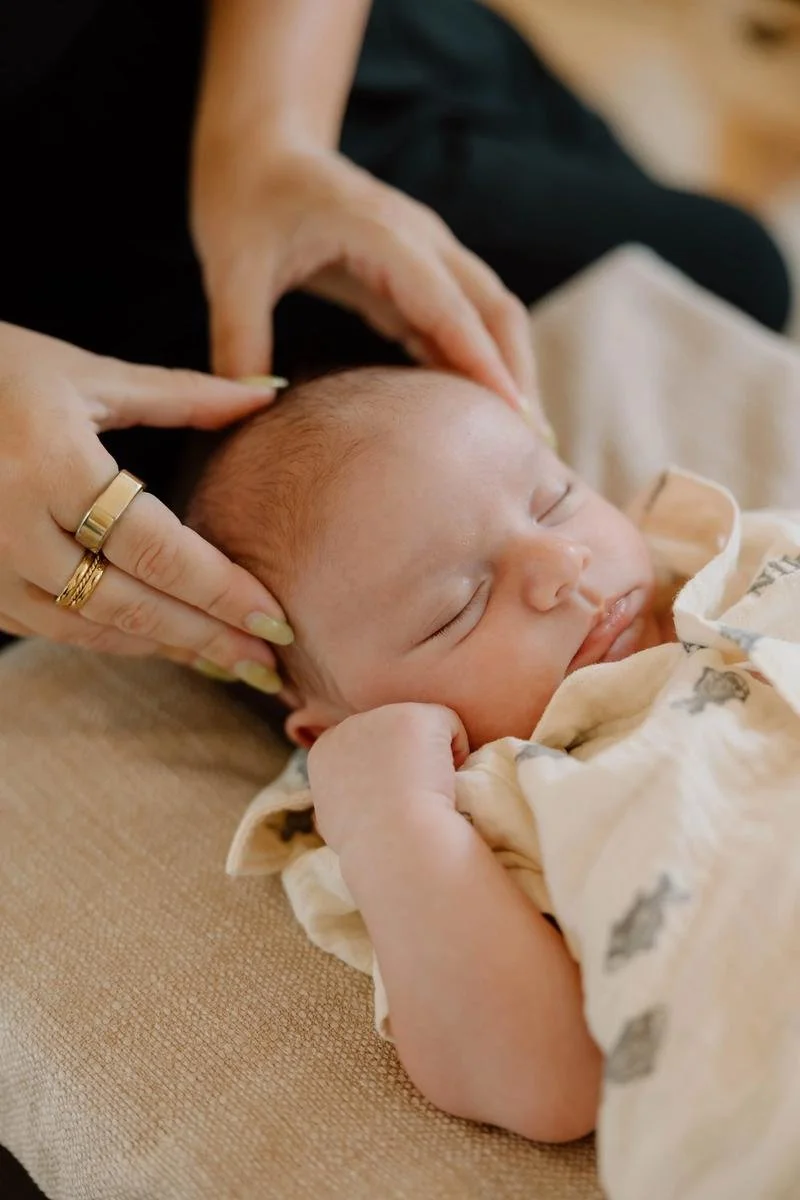 Sleeping newborn receiving gentle cranial hold during infant chiropractic session, close-up — infant chiropractic care at Free Spirit Chiropractic in Tulsa