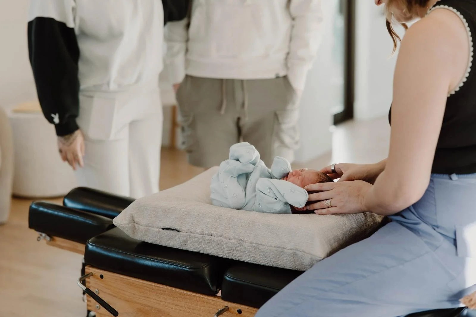 Chiropractor adjusting newborn on support pillow while toddler sister watches from beside the table — pediatric chiropractor in Tulsa, Oklahoma