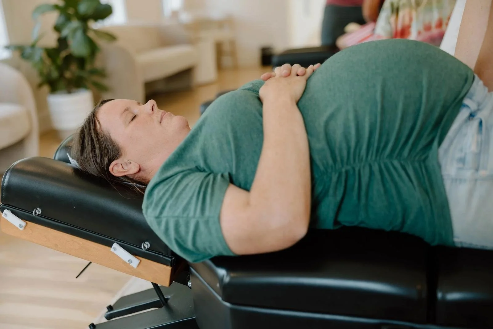 Pregnant patient in green top lying supine on adjustment table with belly visible — Webster Technique prenatal chiropractor in Tulsa