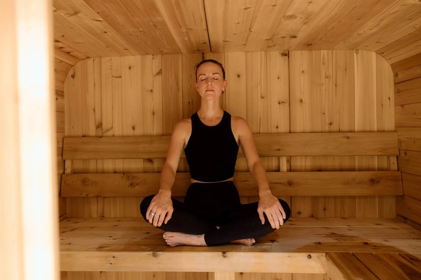 Woman meditating cross-legged in wooden infrared sauna at ADAPT Tulsa, the wellness sister facility to Free Spirit Chiropractic